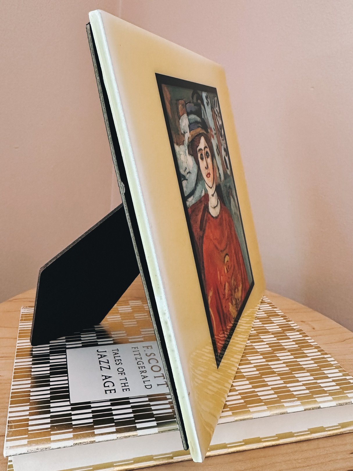 Ceramic portrait titled "La fille aux yeux verts" by Matisse, featuring a woman in a red garment, displayed on a stack of books against a neutral backdrop.