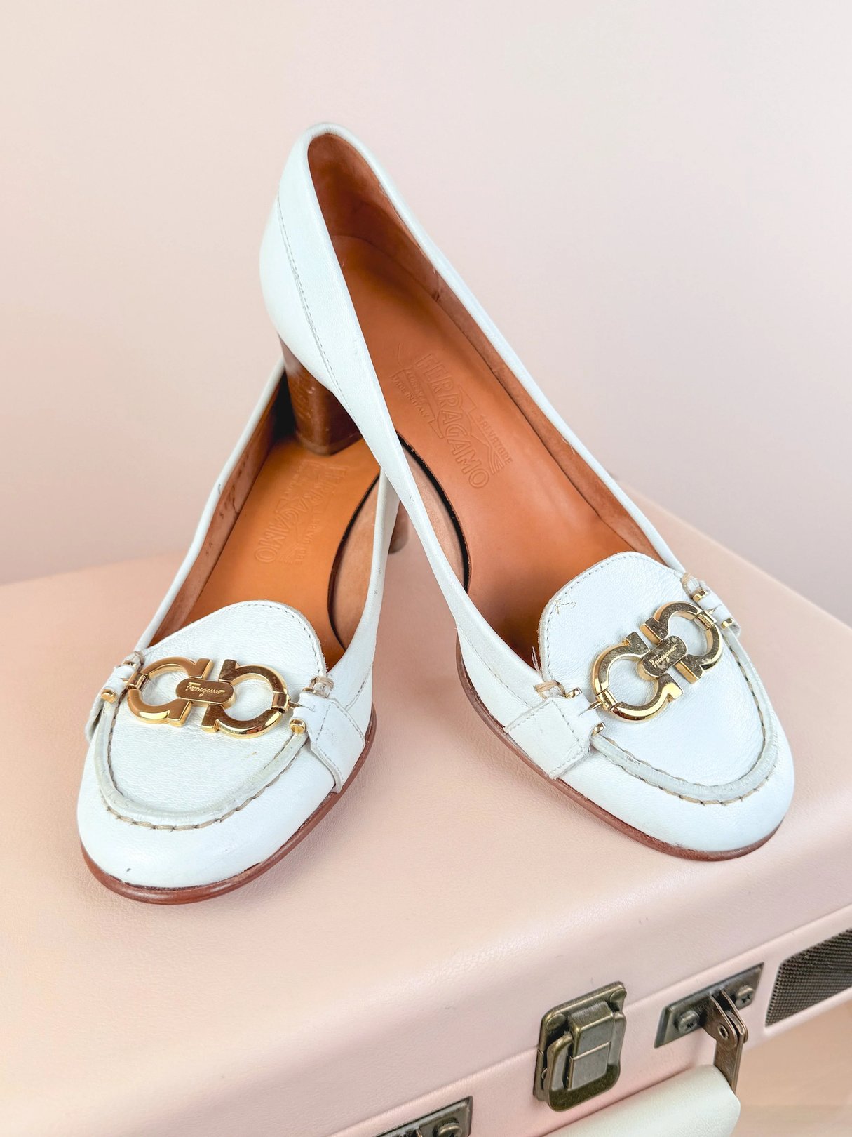 A pair of white leather loafers with a gold decorative buckle on the front.