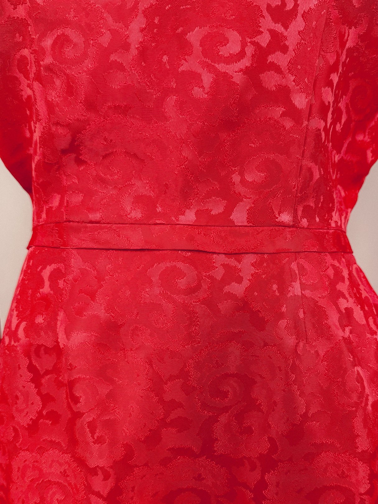 A close-up view of a red damask dress featuring a textured floral pattern, tailored for women in the 1950s.