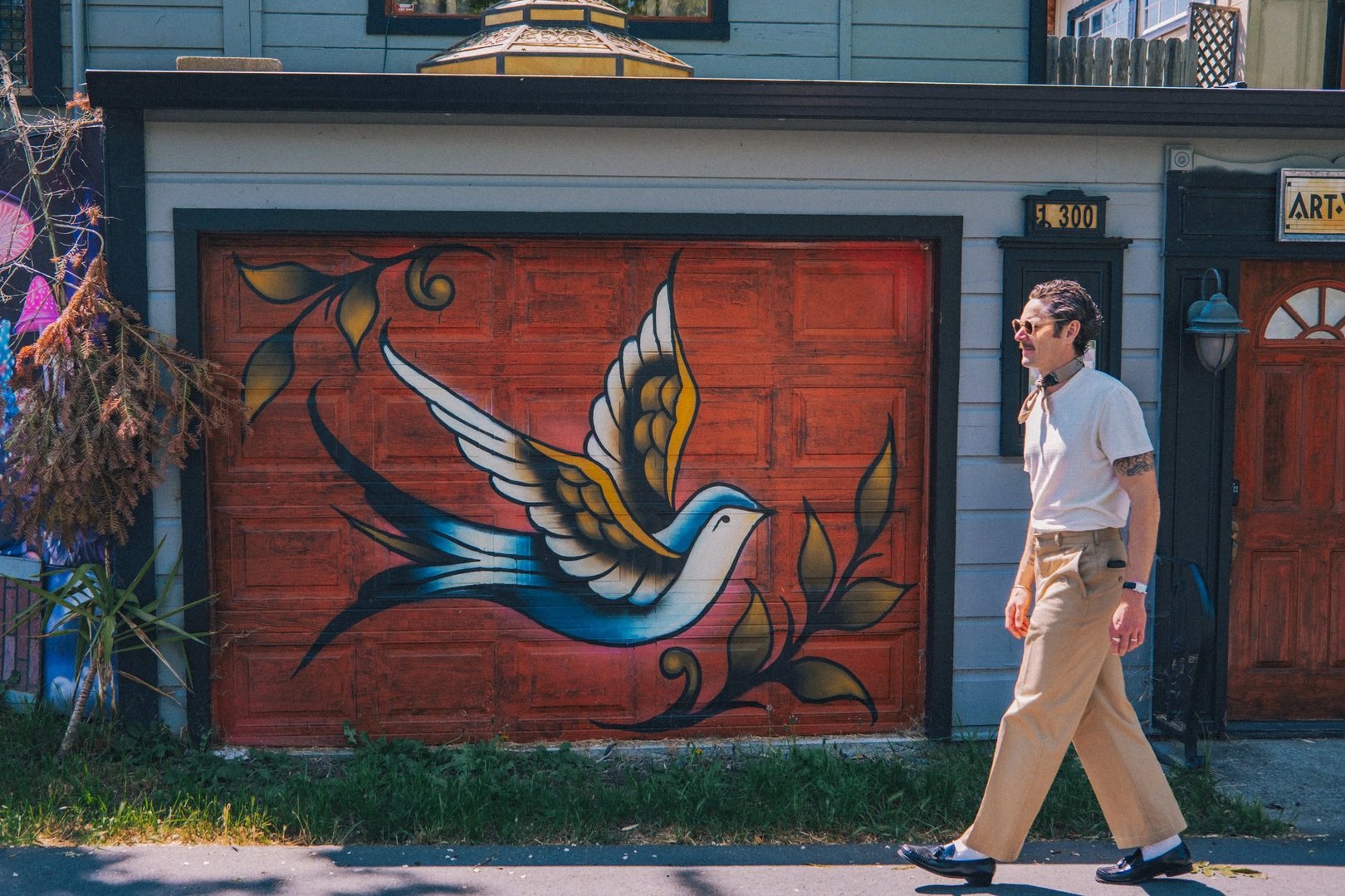 A person walks past a vibrant mural of a bird on a red garage door.