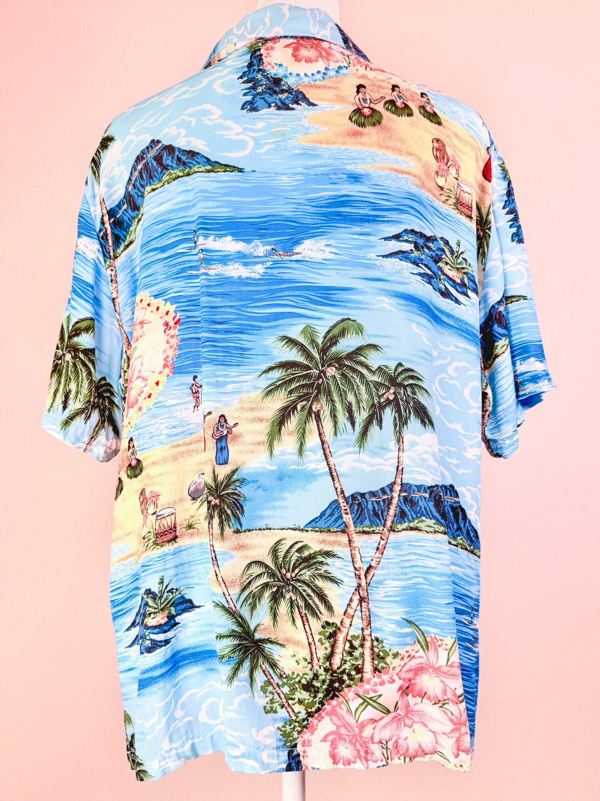 1960s women's blue Aloha Darling Top featuring a tropical beach scene with palm trees and hula dancers.