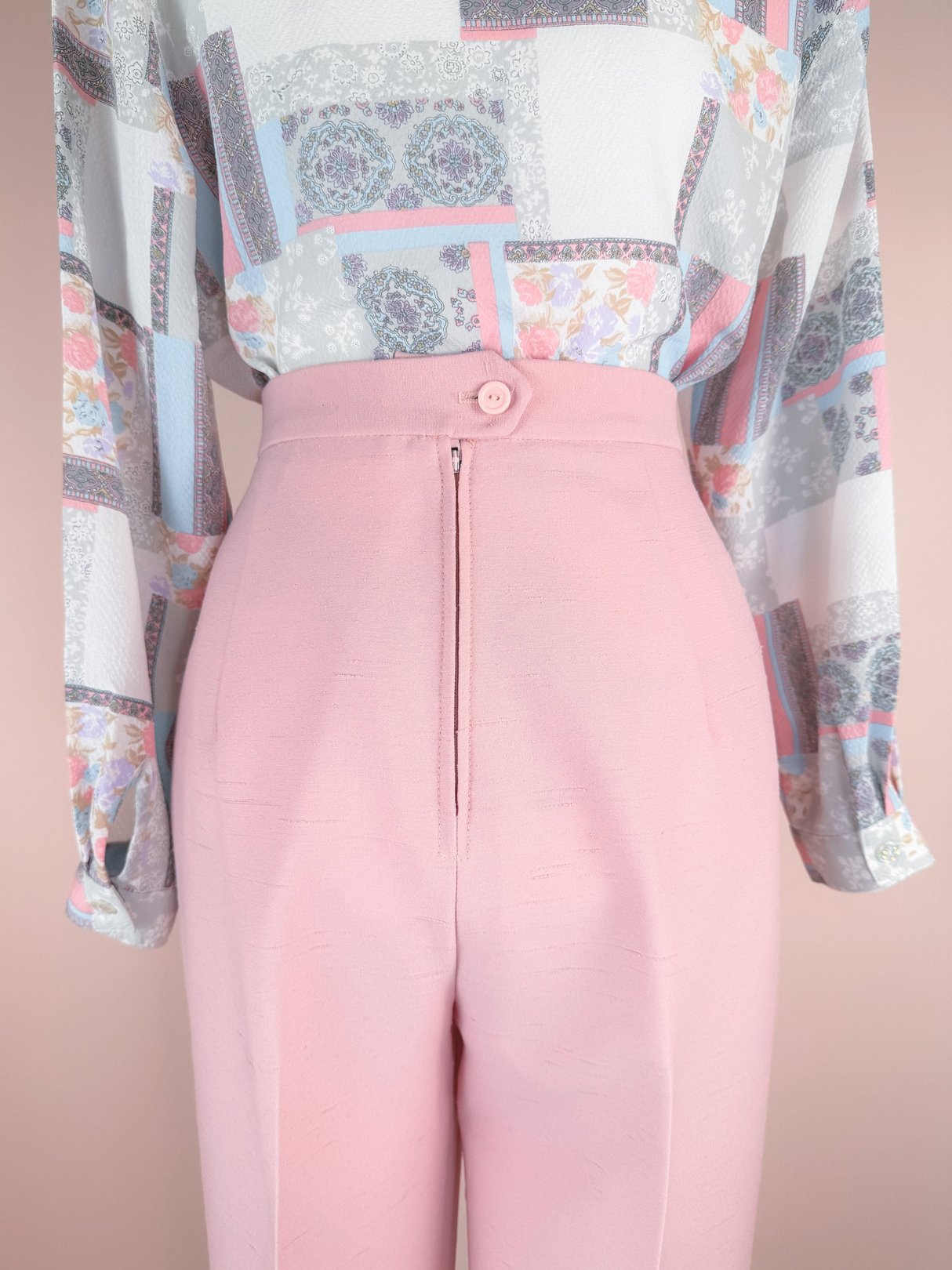 Blush pink high-waisted pants with a back zipper and button closure, styled with a patterned blouse featuring floral and geometric designs.