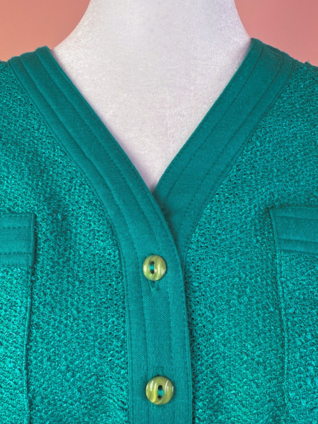 Teal knitted dress featuring a V-neckline, textured fabric, and two front pockets with contrasting buttons.