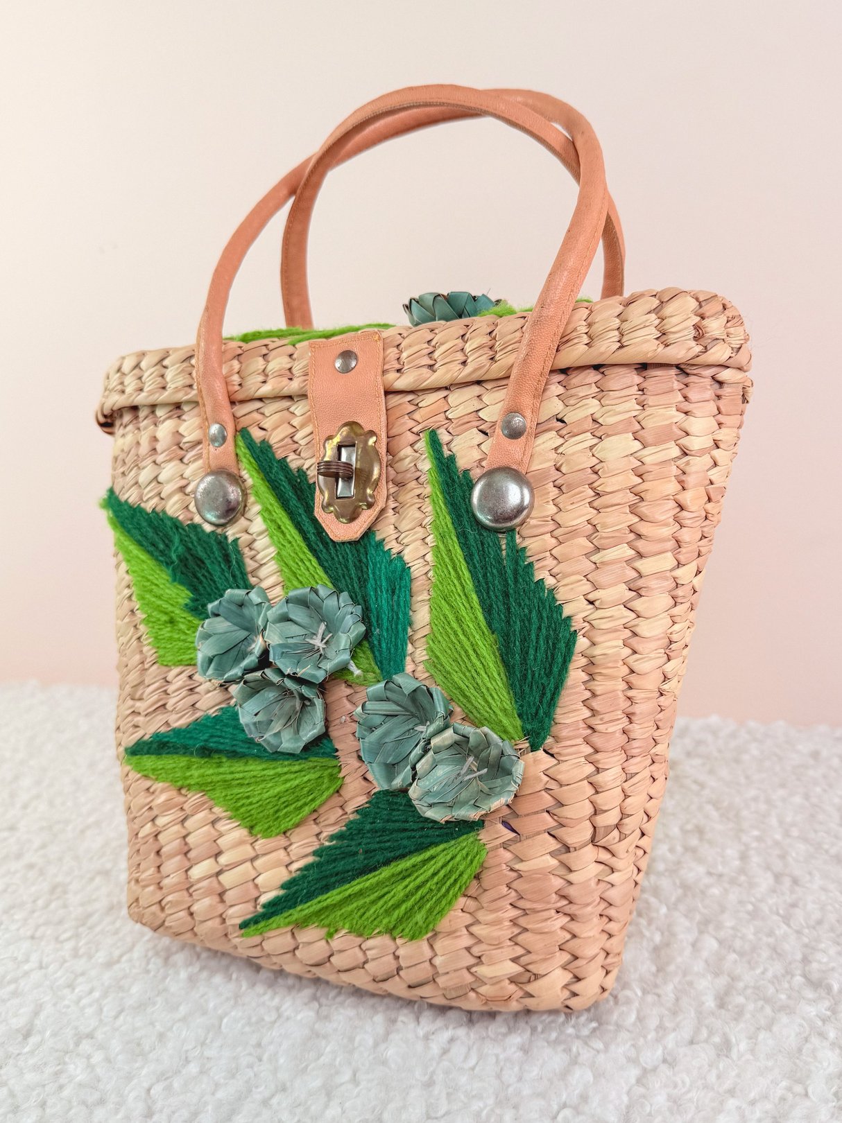 Woven straw handbag featuring green and blue floral accents, designed for women, reflecting a 1970s style.