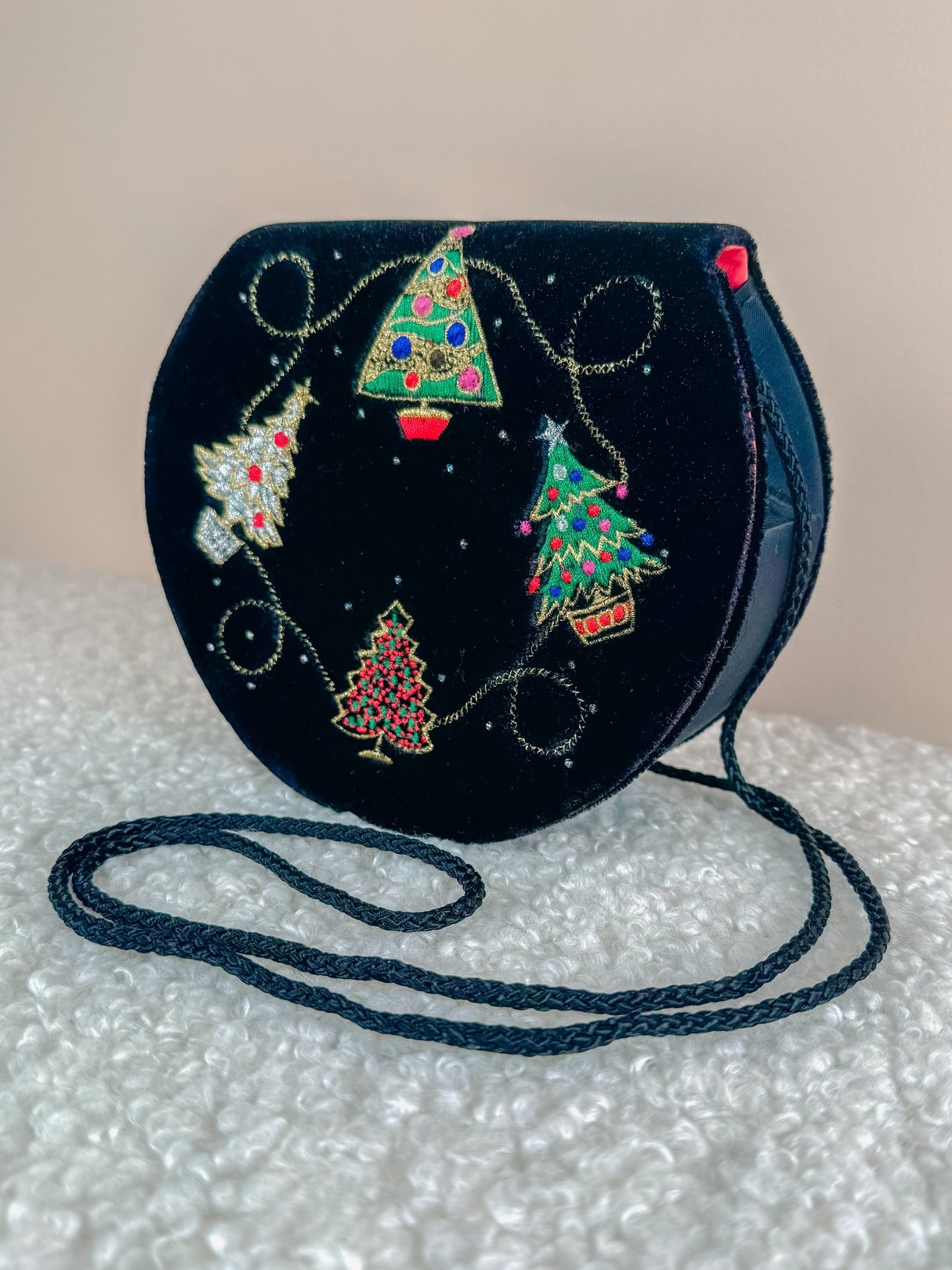 Round black velvet purse featuring colorful Christmas tree embroidery and a long black strap.