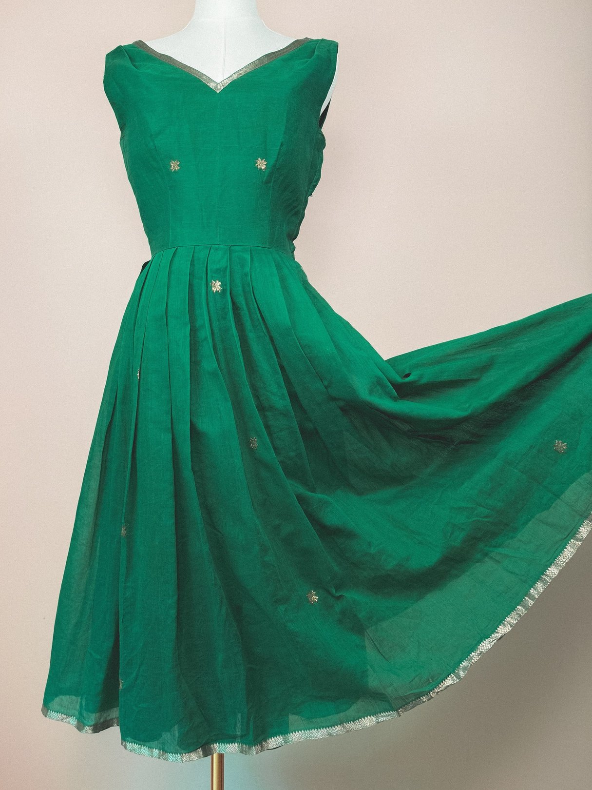 A 1950s-styled emerald green dress featuring a pleated skirt and subtle gold embellishments.