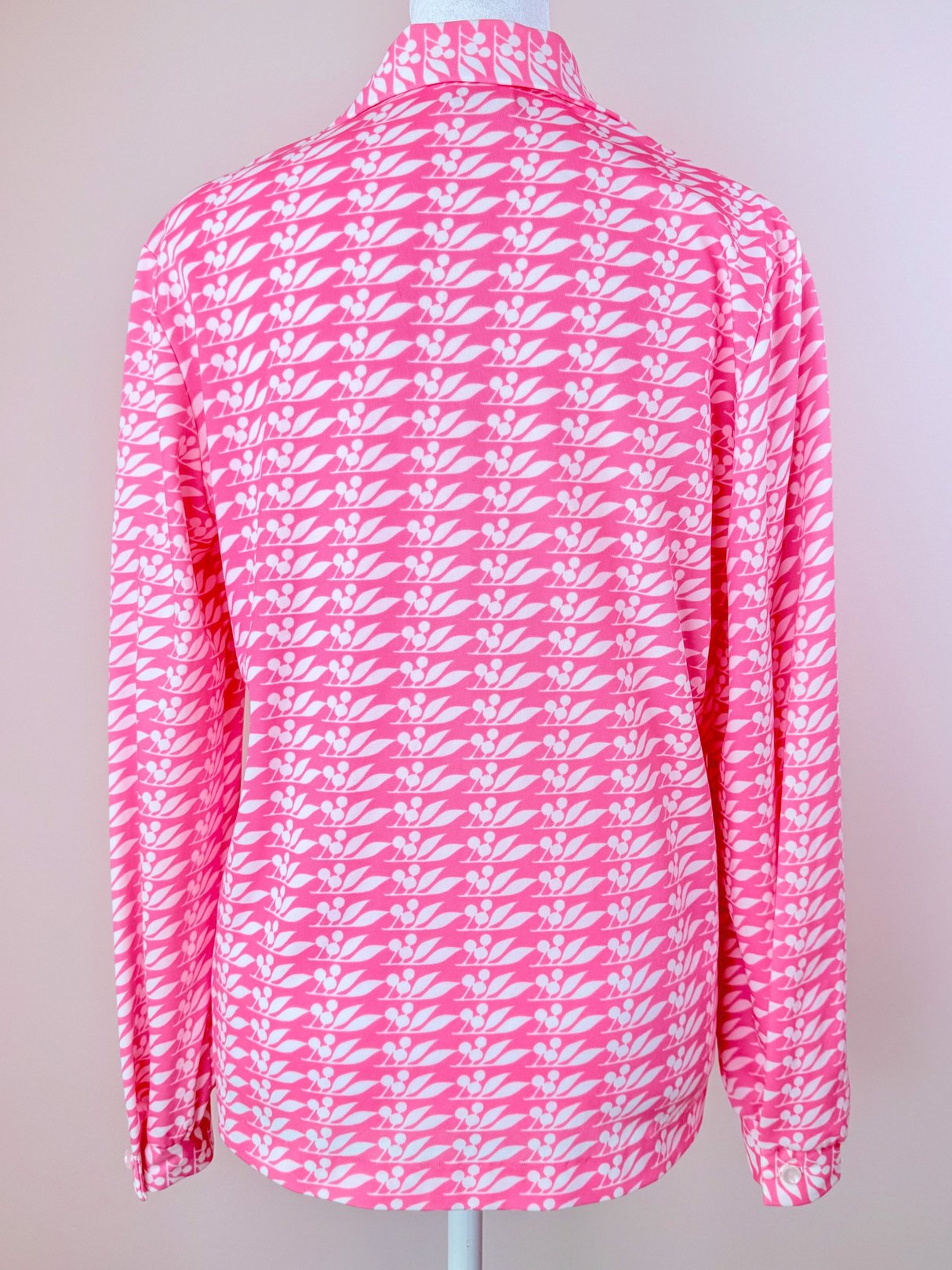 The Cherry Petal Blouse features a 1970s design with a pink floral pattern, long sleeves, and a collared neck, showcased from the back.