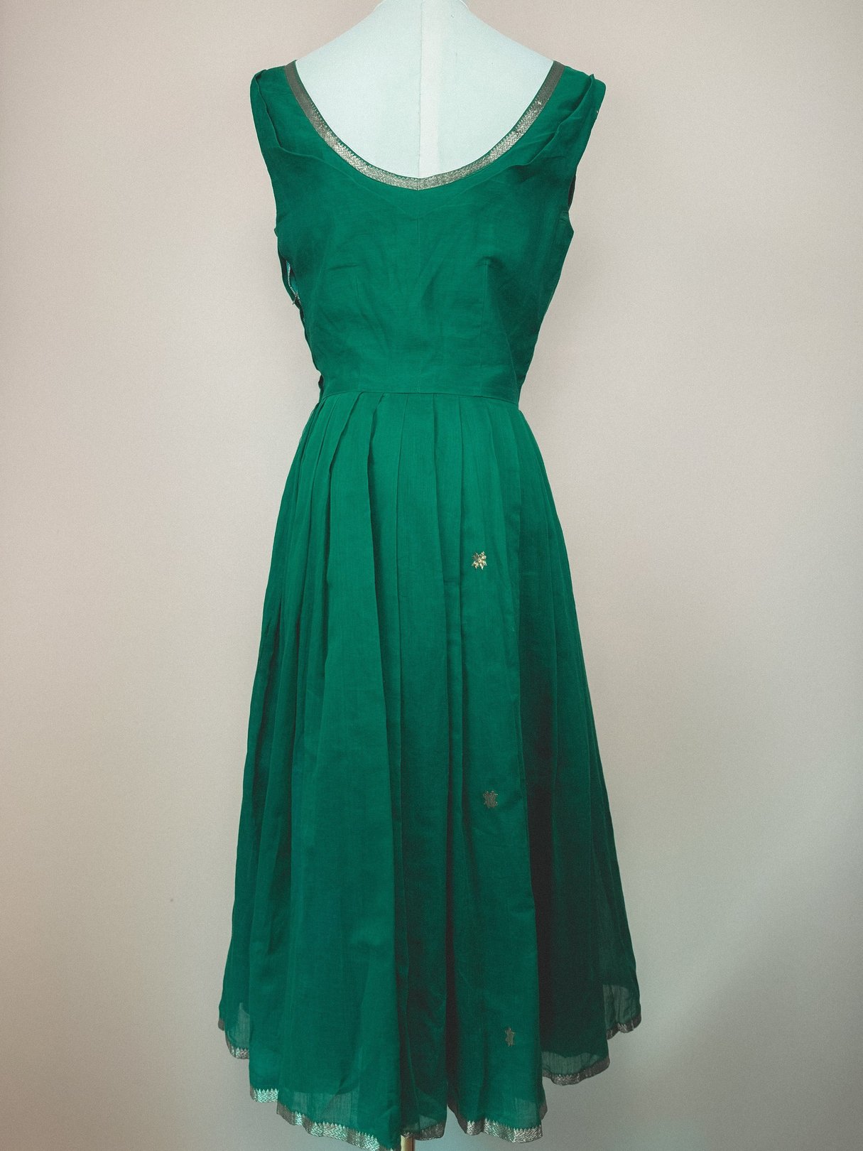 Green 1950s women’s dress featuring a sleeveless design, flared skirt, and decorative starburst embellishments.