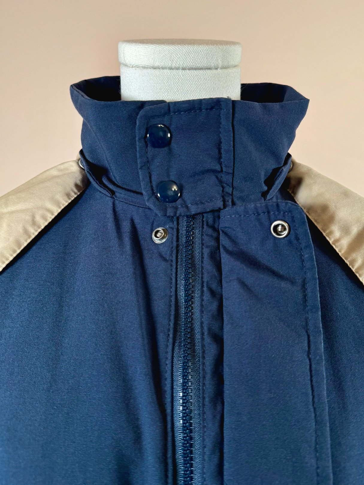 Navy utility field coat for women featuring a high collar and contrasting tan shoulder panels, styled with a zip closure and snap buttons, reflecting 1970s fashion.