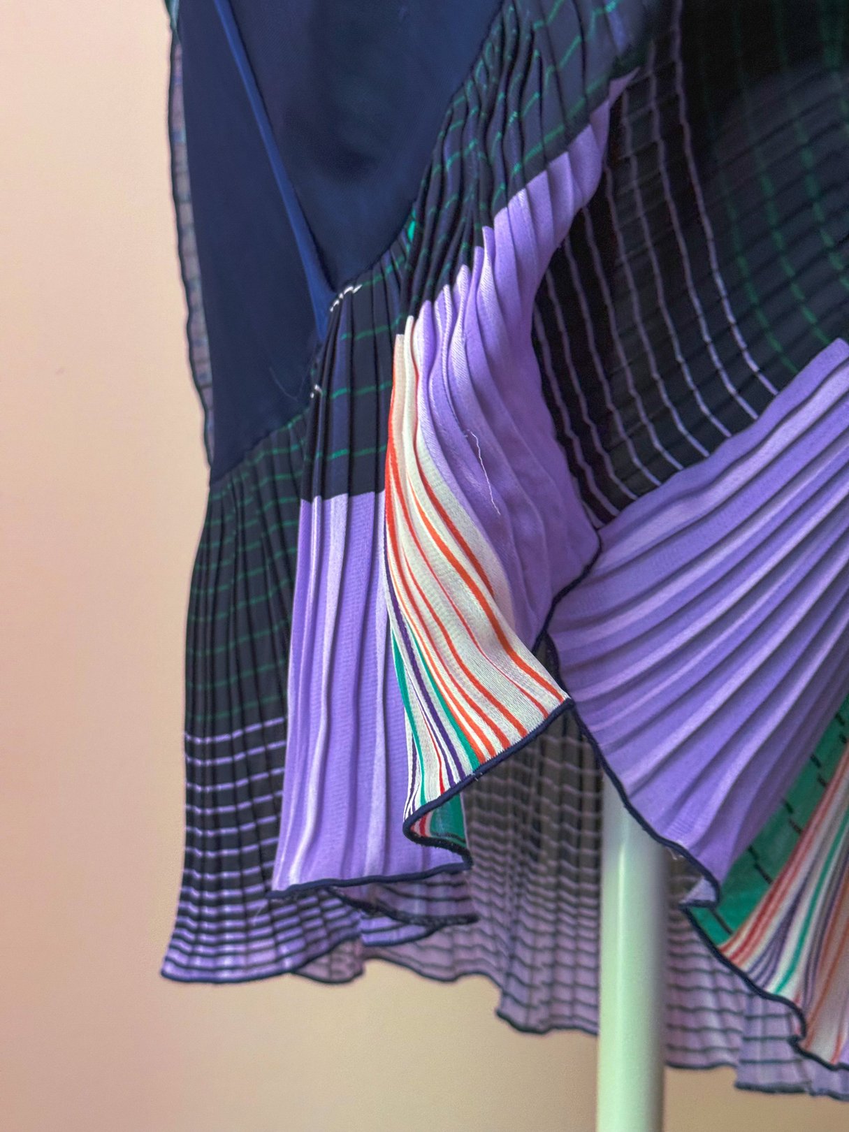 The Off The Grid Pleated Skirt features a mix of green and purple pleated fabrics with striped accents, reflecting a 1970s style for women.
