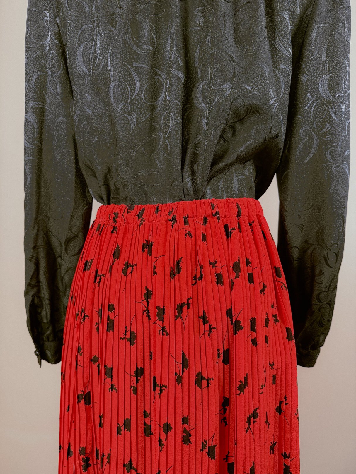 Pleated red skirt featuring a floral pattern, styled with a dark patterned blouse, reflecting a 1970s women's fashion aesthetic.