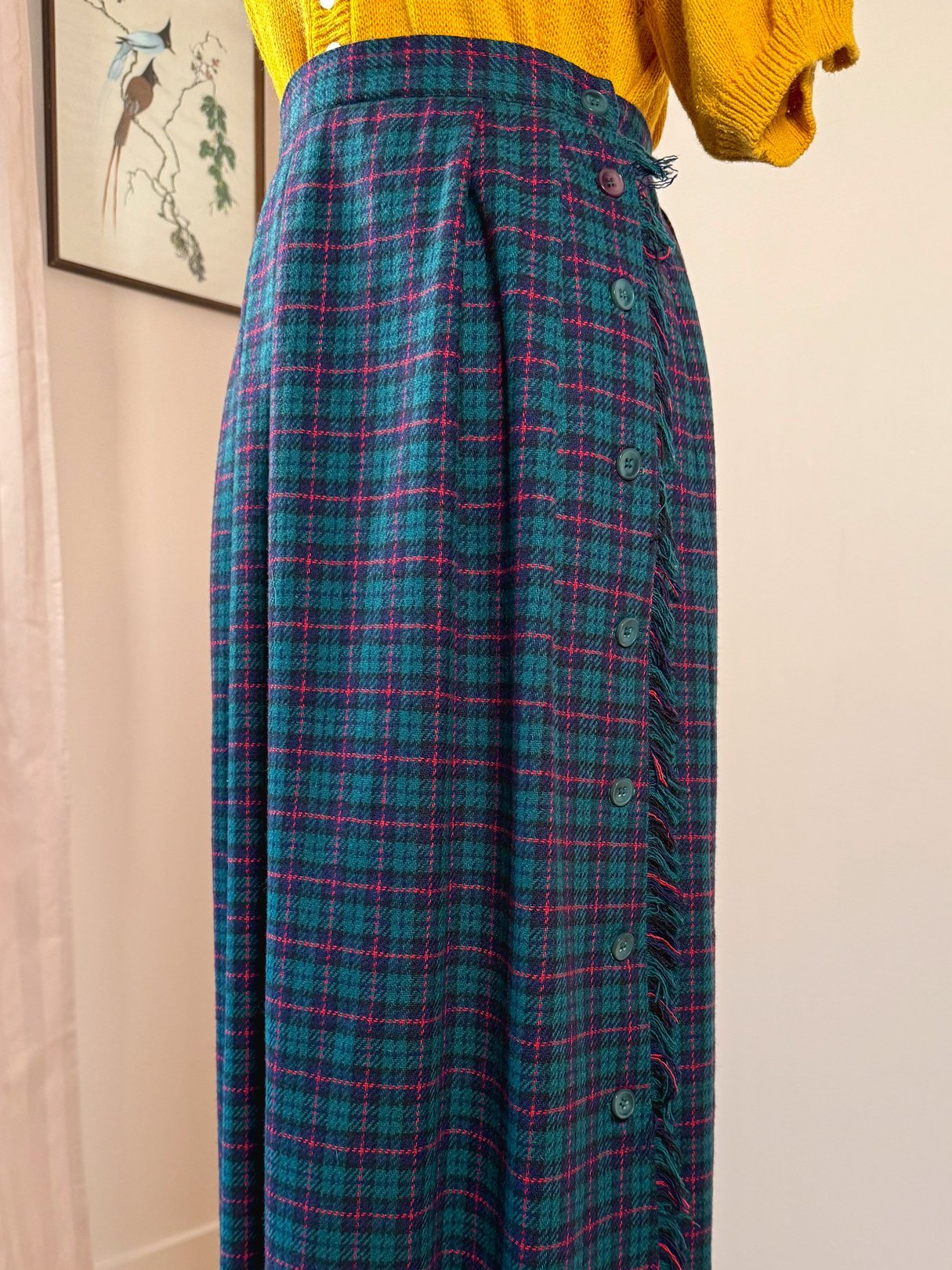 A green plaid skirt featuring a high waist, button details, and a 1970s style.