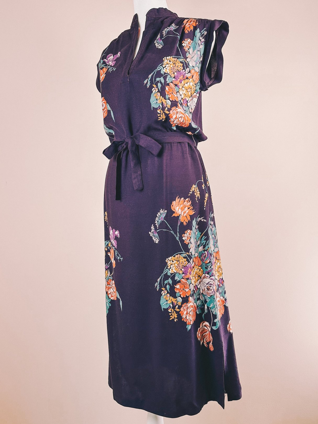 1970s women's dress in purple featuring a floral design and a tie waistband.