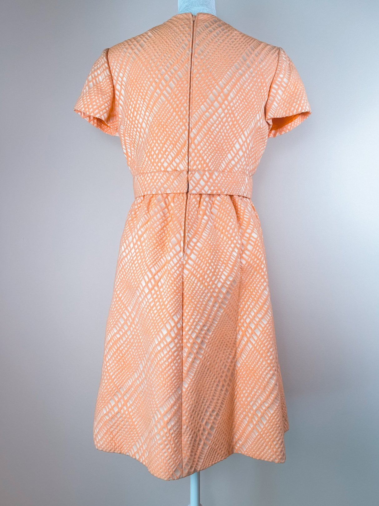 The Orange Jubilee Dress features a fitted bodice, flared skirt, and short sleeves with a textured pattern, representative of 1960s women's fashion.