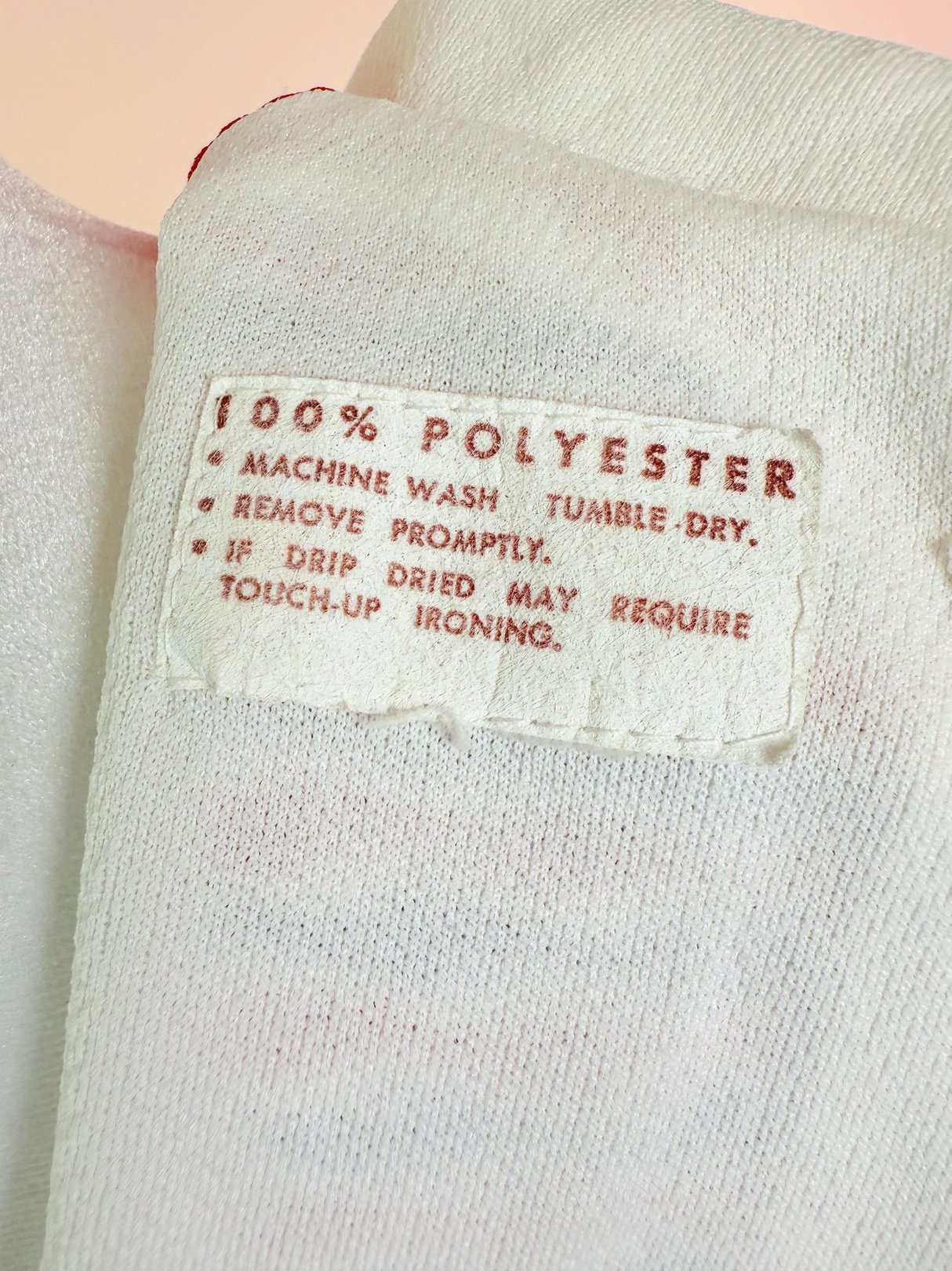 Red 1970s women's Bottle Rocket Dress with a care label indicating 100% polyester material and washing instructions.