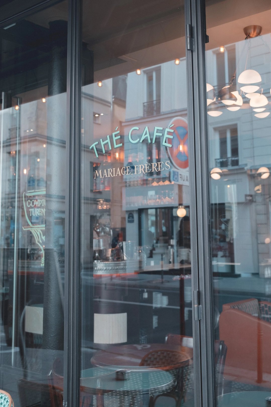 A storefront view of Thé Café Mariage Frères, featuring glass doors and a cozy interior aesthetic.
