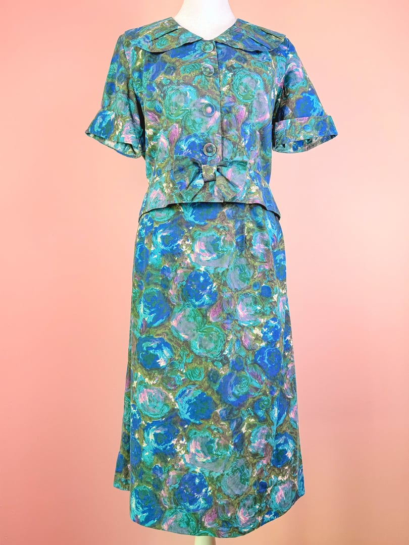 The Coastal Flowers Skirt Set features a blue 1950s-style printed blouse with a collar and short sleeves, paired with a matching skirt that has a fitted waist and flowing silhouett