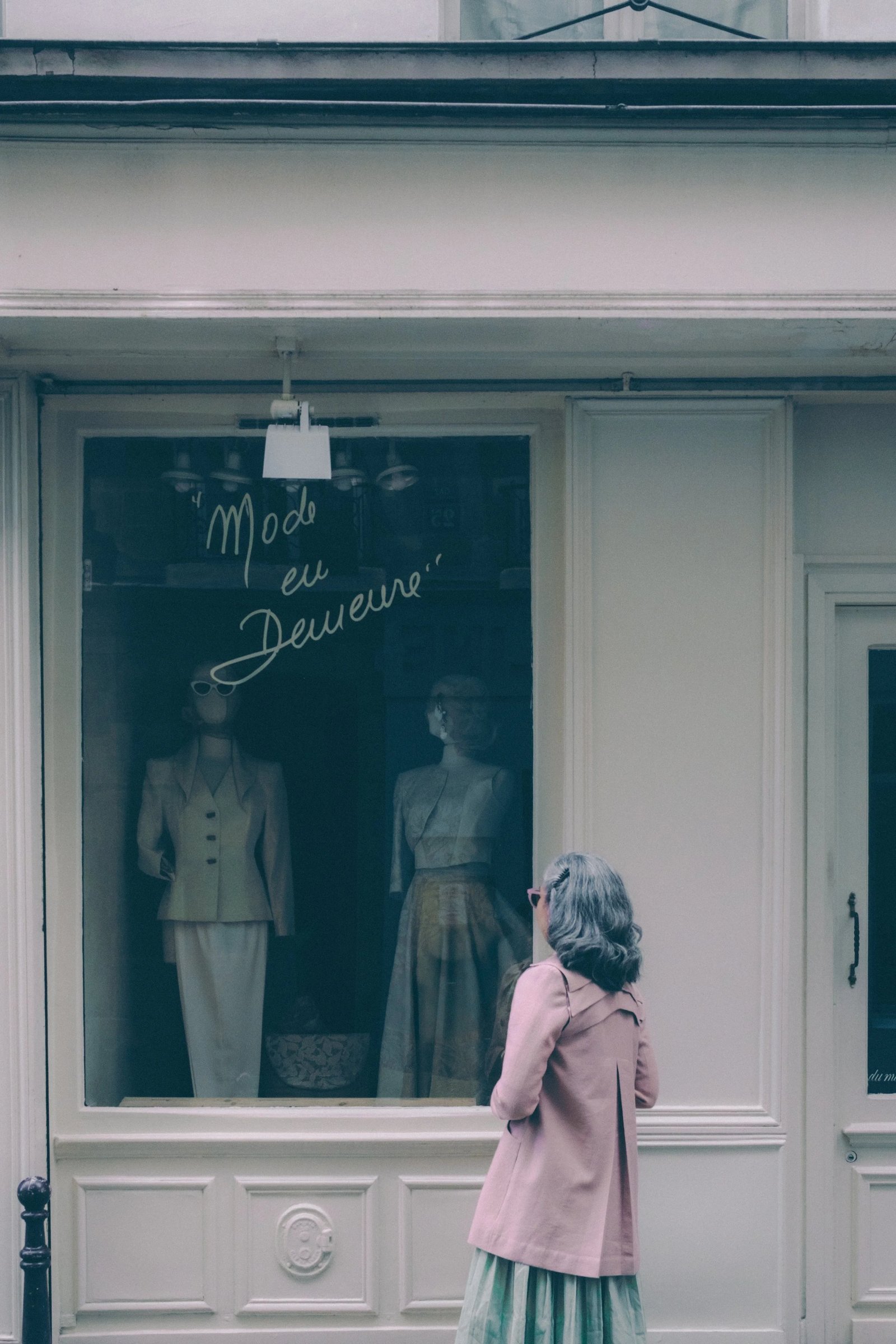 A person walks in front of a storefront featuring mannequins dressed in fashionable clothing.