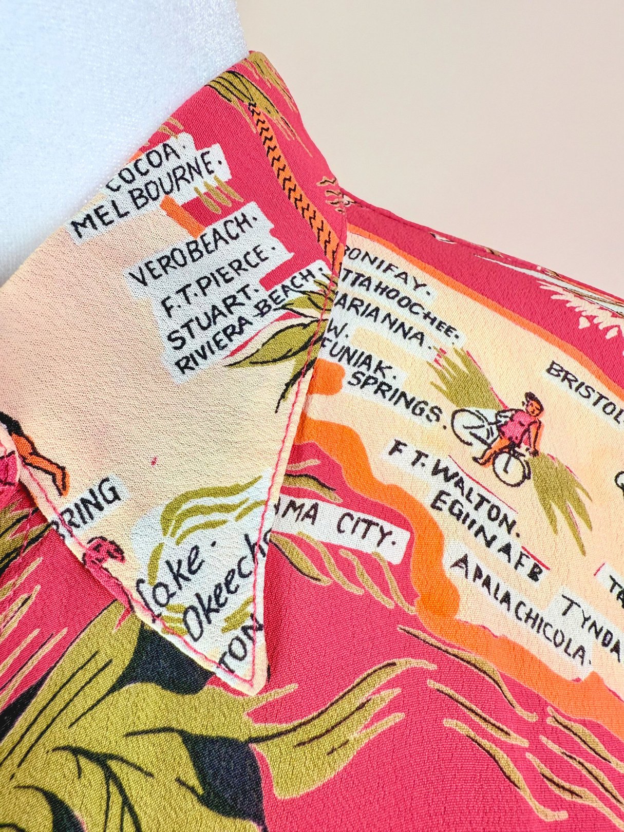 White women’s top from the 1970s featuring a colorful map print with Florida locations and tropical motifs.