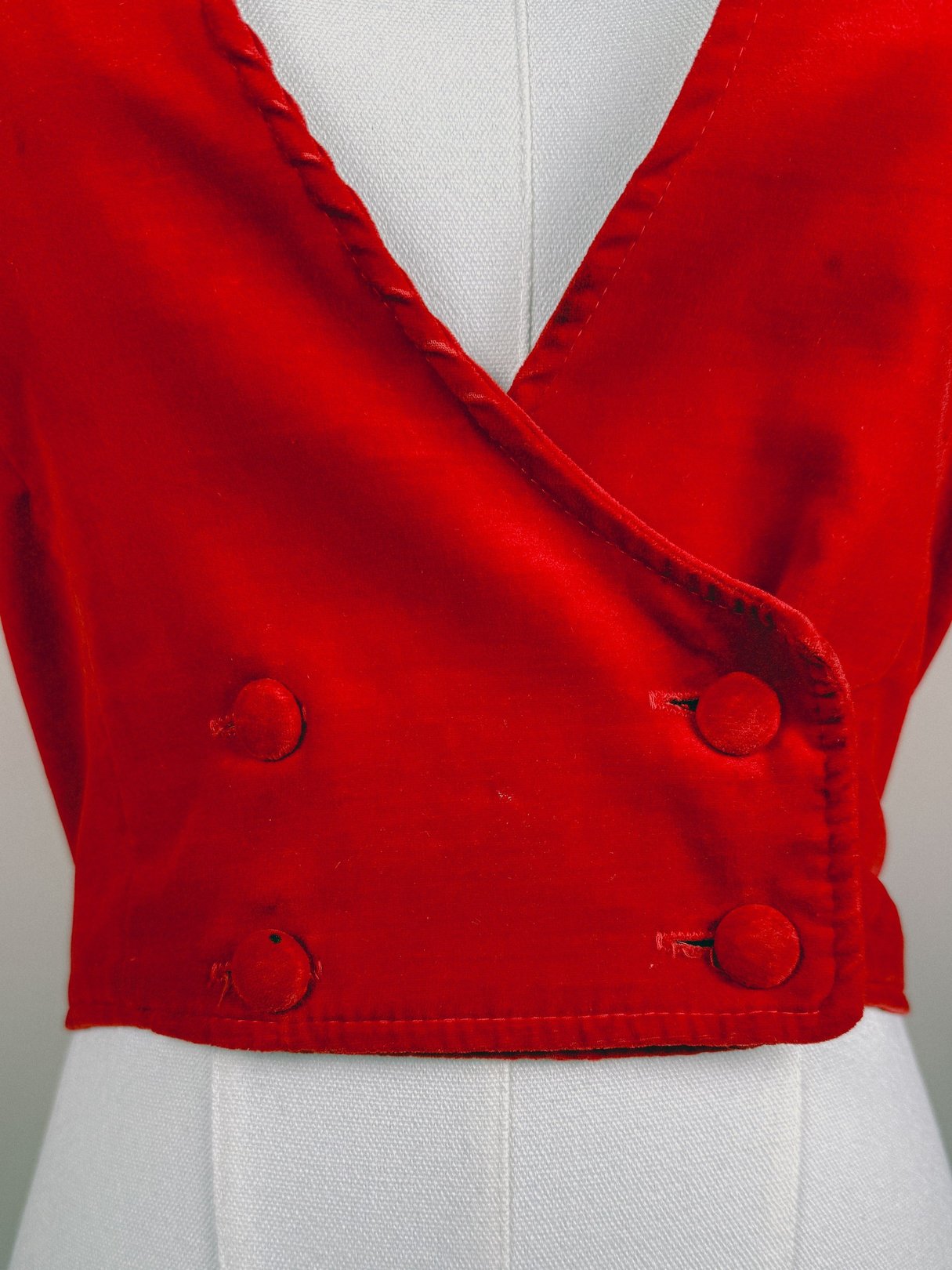 Red velvet vest with a wrap design and two buttons, representing 1970s women's fashion.