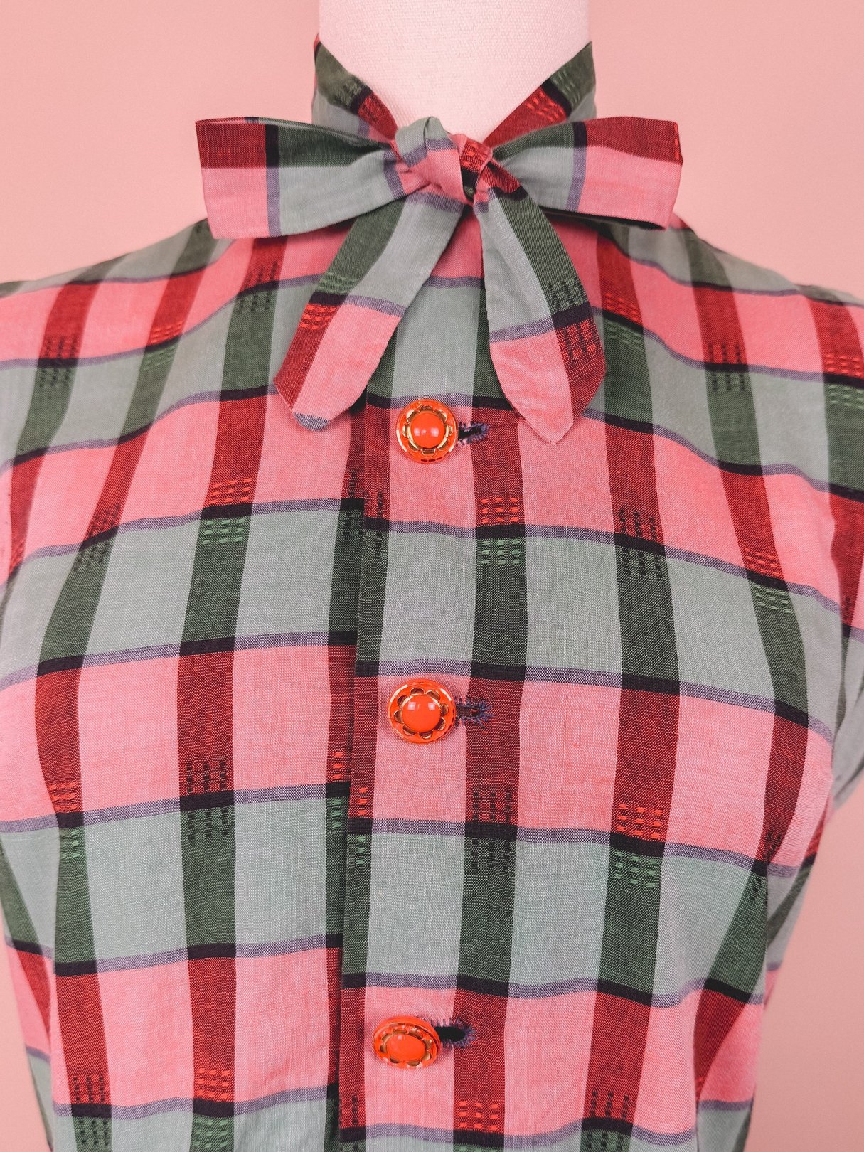 Red and green plaid dress with a bow collar and orange buttons, reflecting 1950s style.