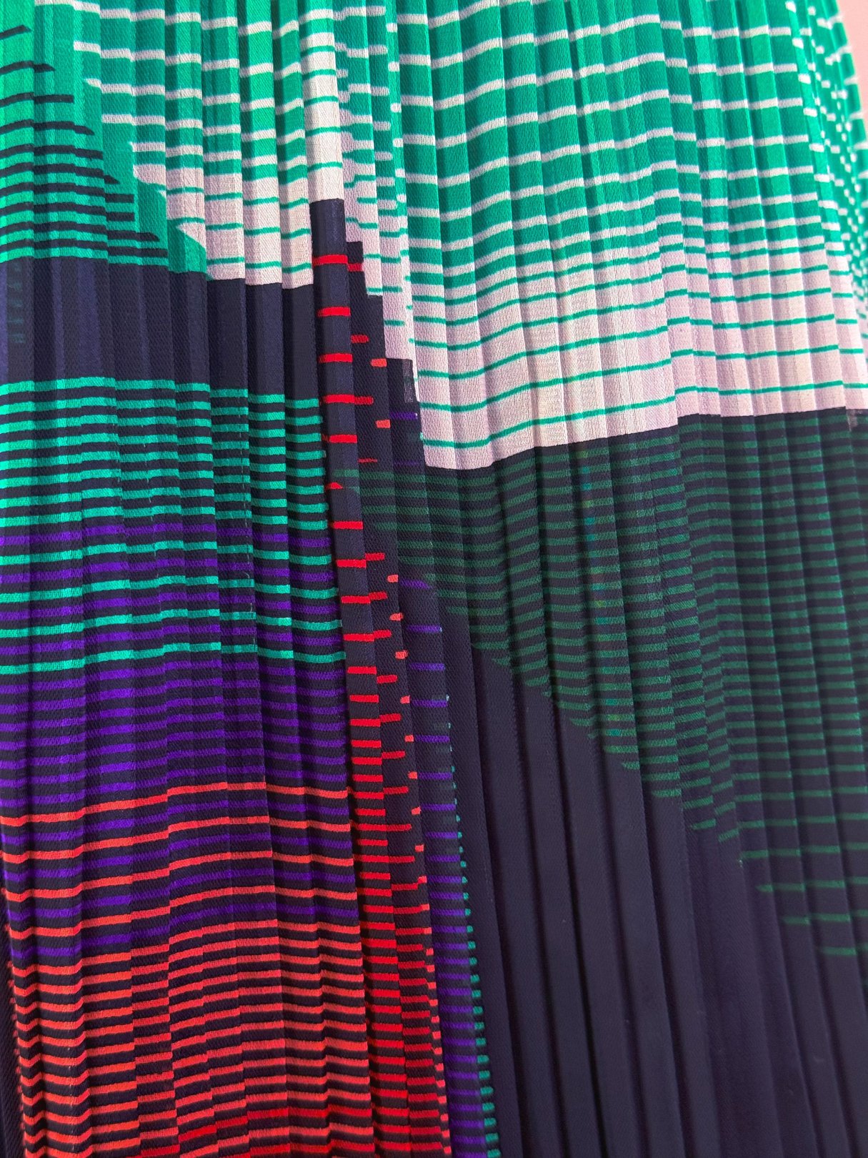 Green pleated skirt featuring a bold 1970s-inspired geometric print in various colors.