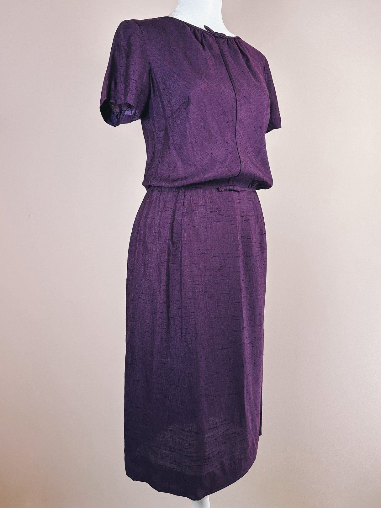 Fitted purple dress with short sleeves, a gathered waist, and a knee-length silhouette, inspired by 1960s fashion.