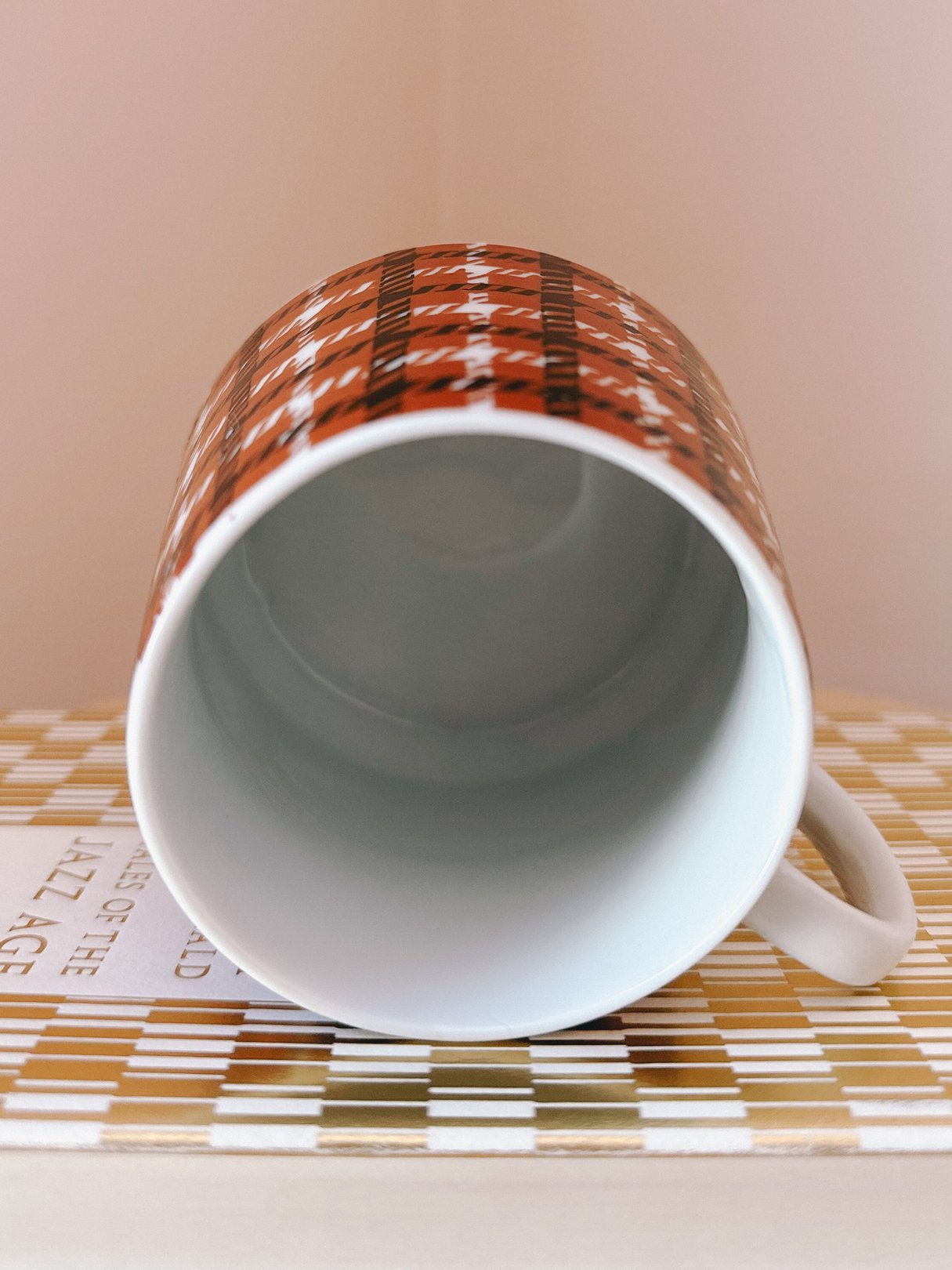 A black and orange houndstooth print mug from the 1970s, featuring a glossy interior and a curved handle, placed on top of a book.