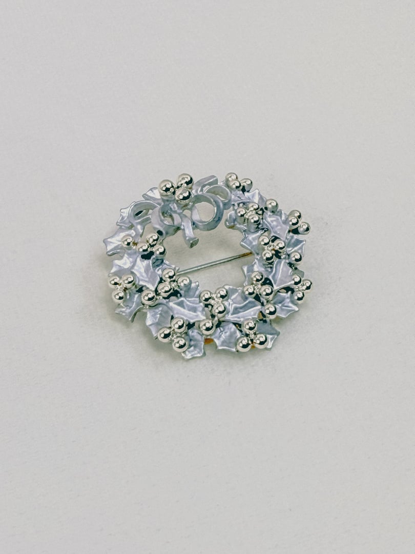 A silver keepsake wreath brooch from the 1970s featuring decorative floral elements and a bow.