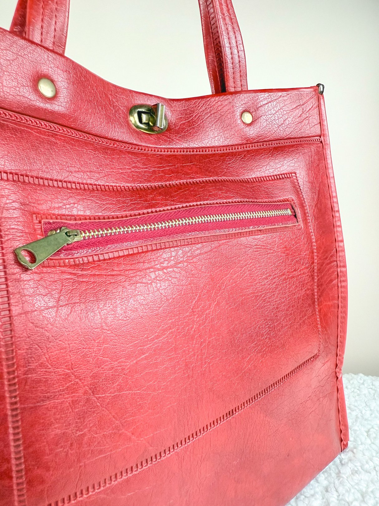 A vibrant red satchel tote with a textured finish, featuring a front zipper pocket and sturdy shoulder straps, reflective of 1970s design.