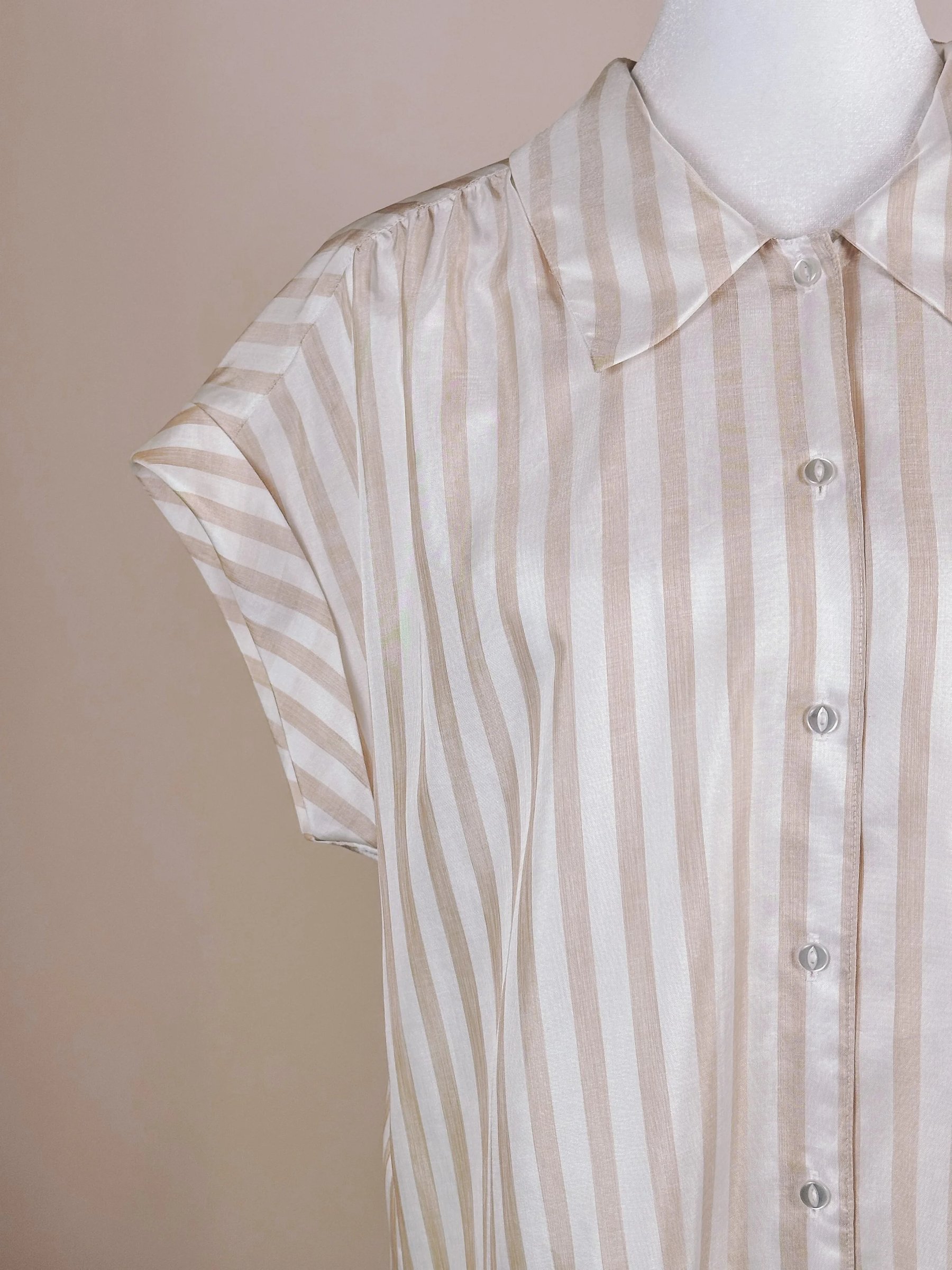 Light beige and white striped short-sleeve shirt with a button-up front and a collar.