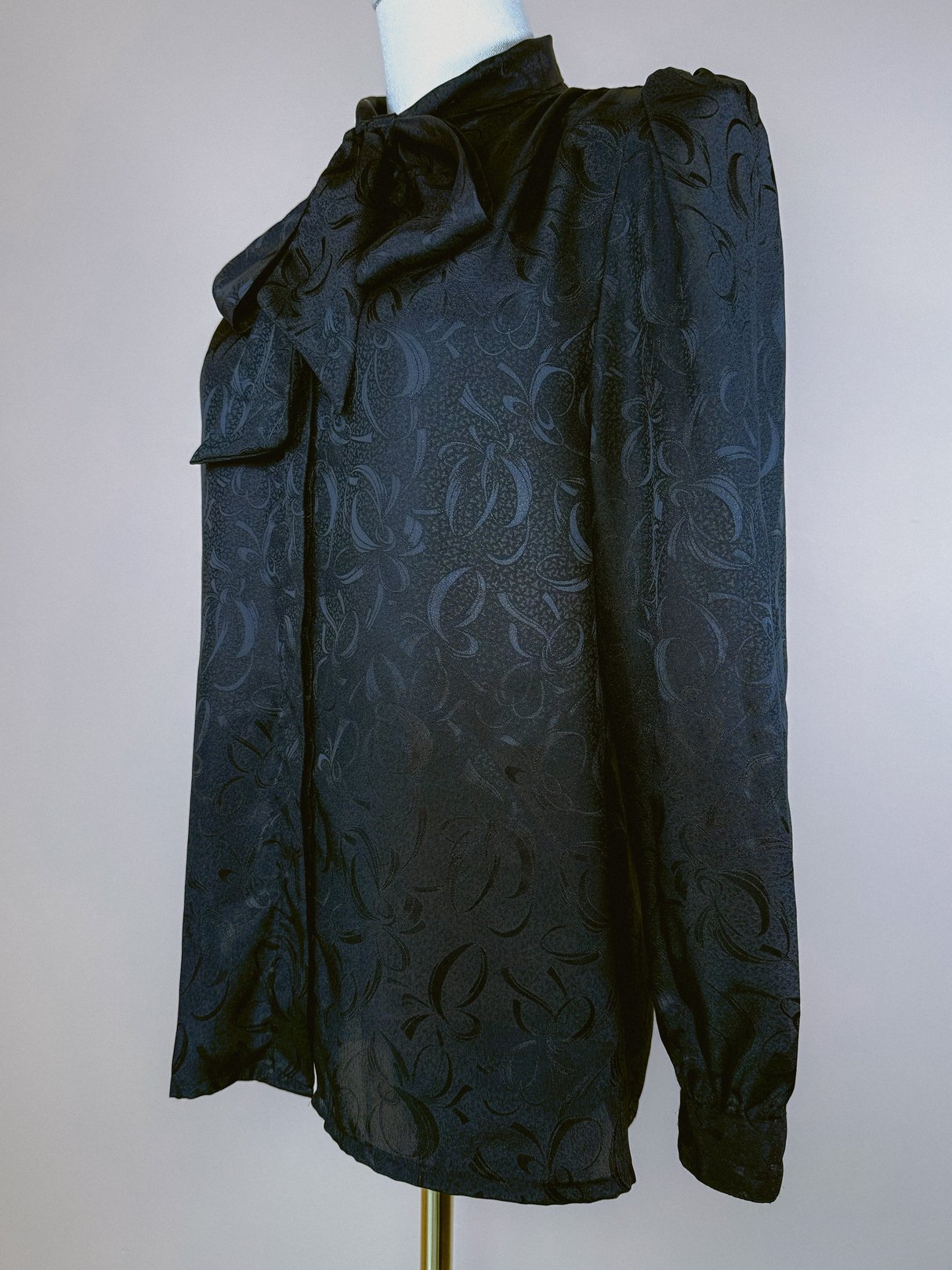 A black long-sleeve top from the 1980s featuring a bow detail at the neckline and a textured floral pattern.