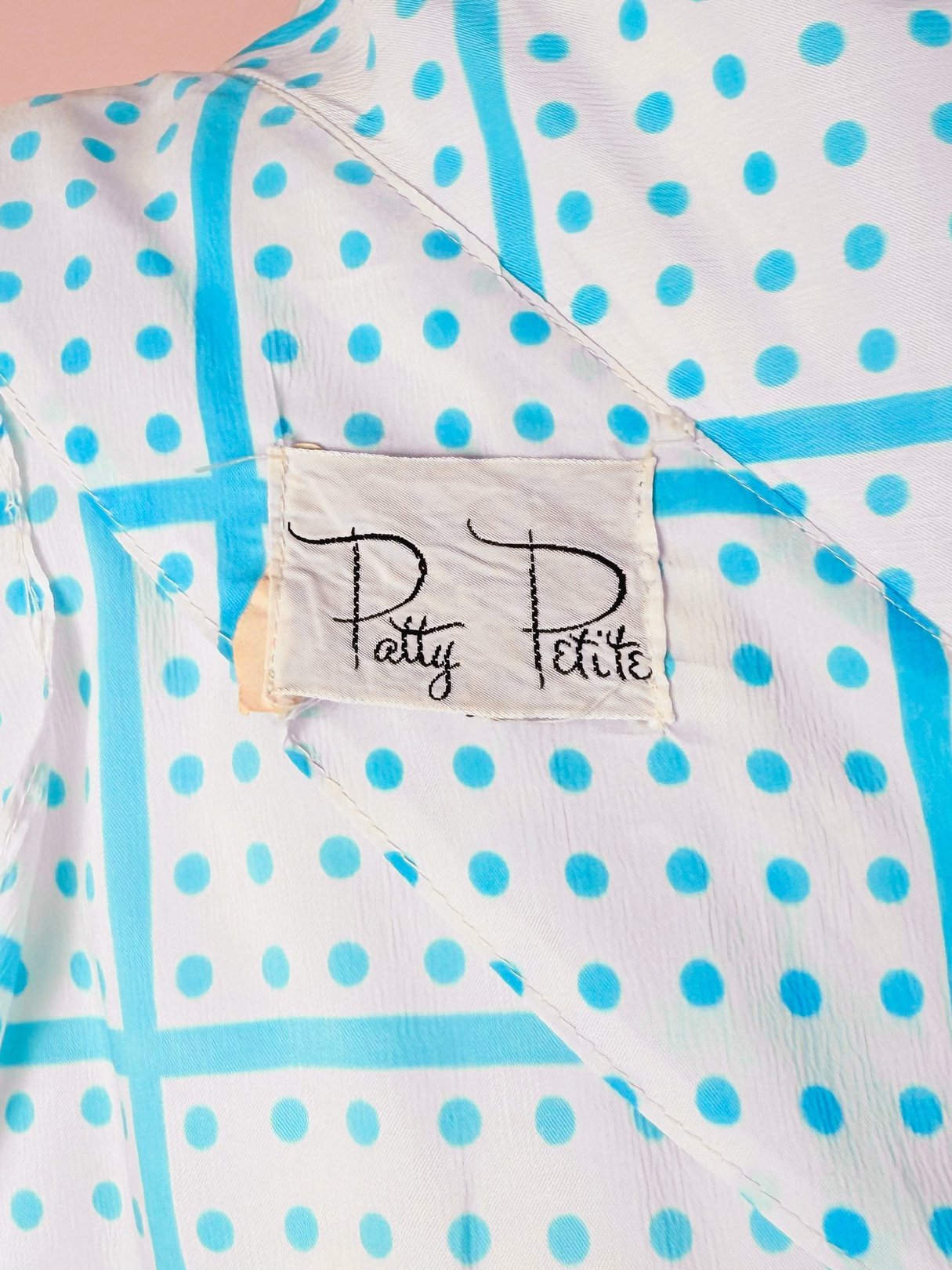 White 1970s women's dress with blue polka dot pattern and a label reading "Patty Petite.