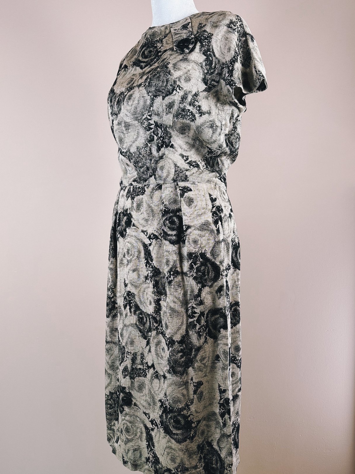 A vintage 1950s women's dress featuring a black and cream rose pattern with a fitted silhouette and short sleeves.