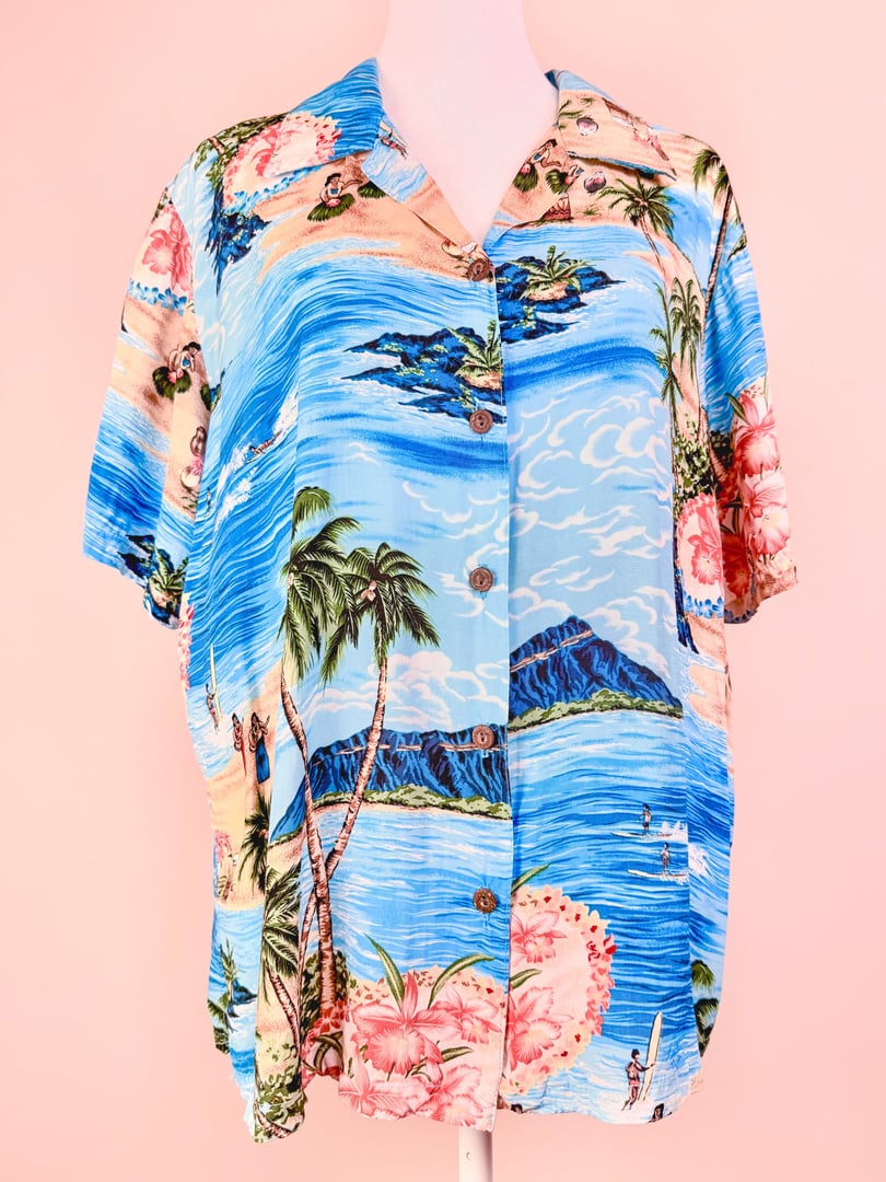 1960s blue Aloha Darling Top for women featuring a tropical landscape design with palm trees and mountains.