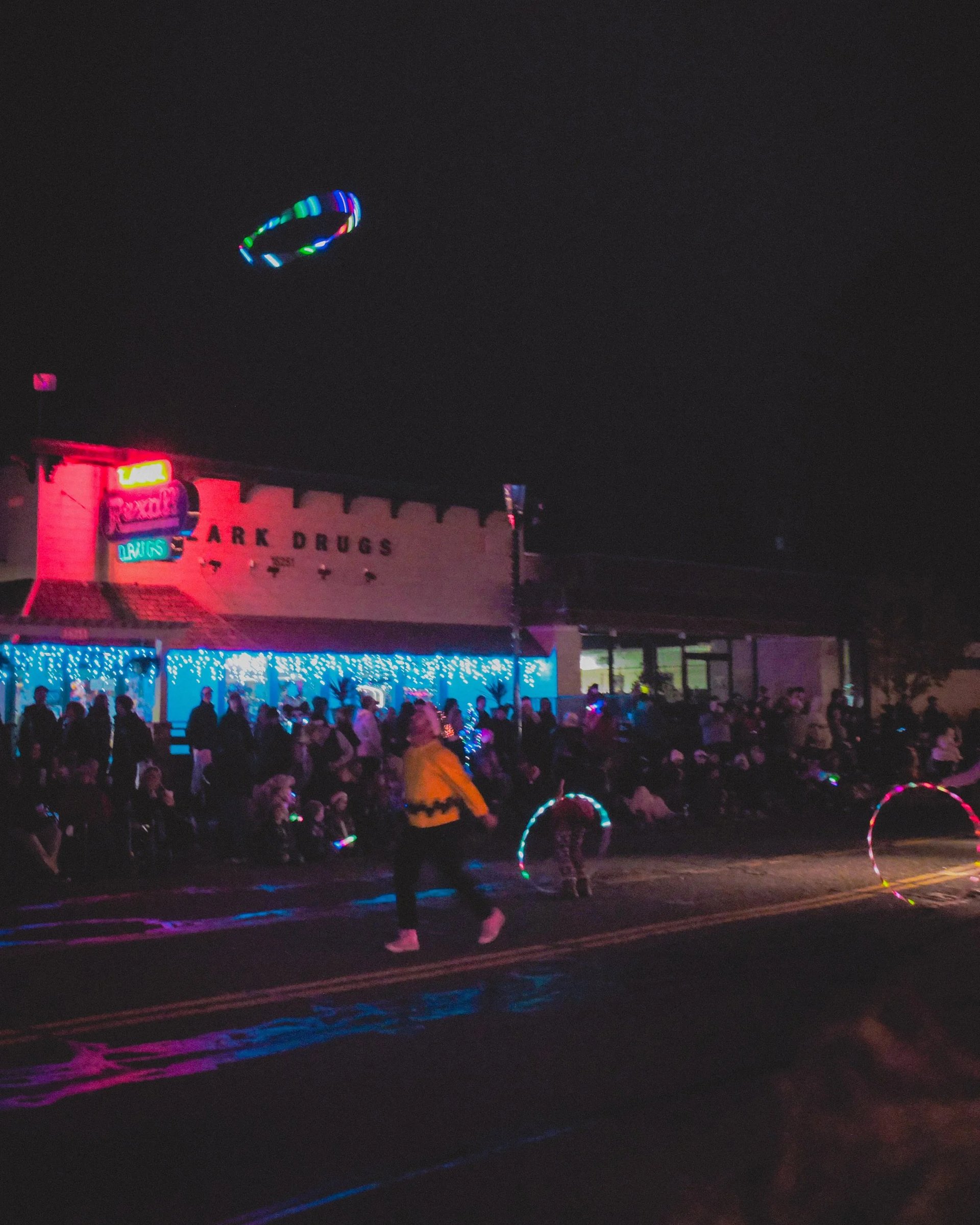 A vibrant nighttime scene featuring a crowd outside a colorful building illuminated by neon lights.