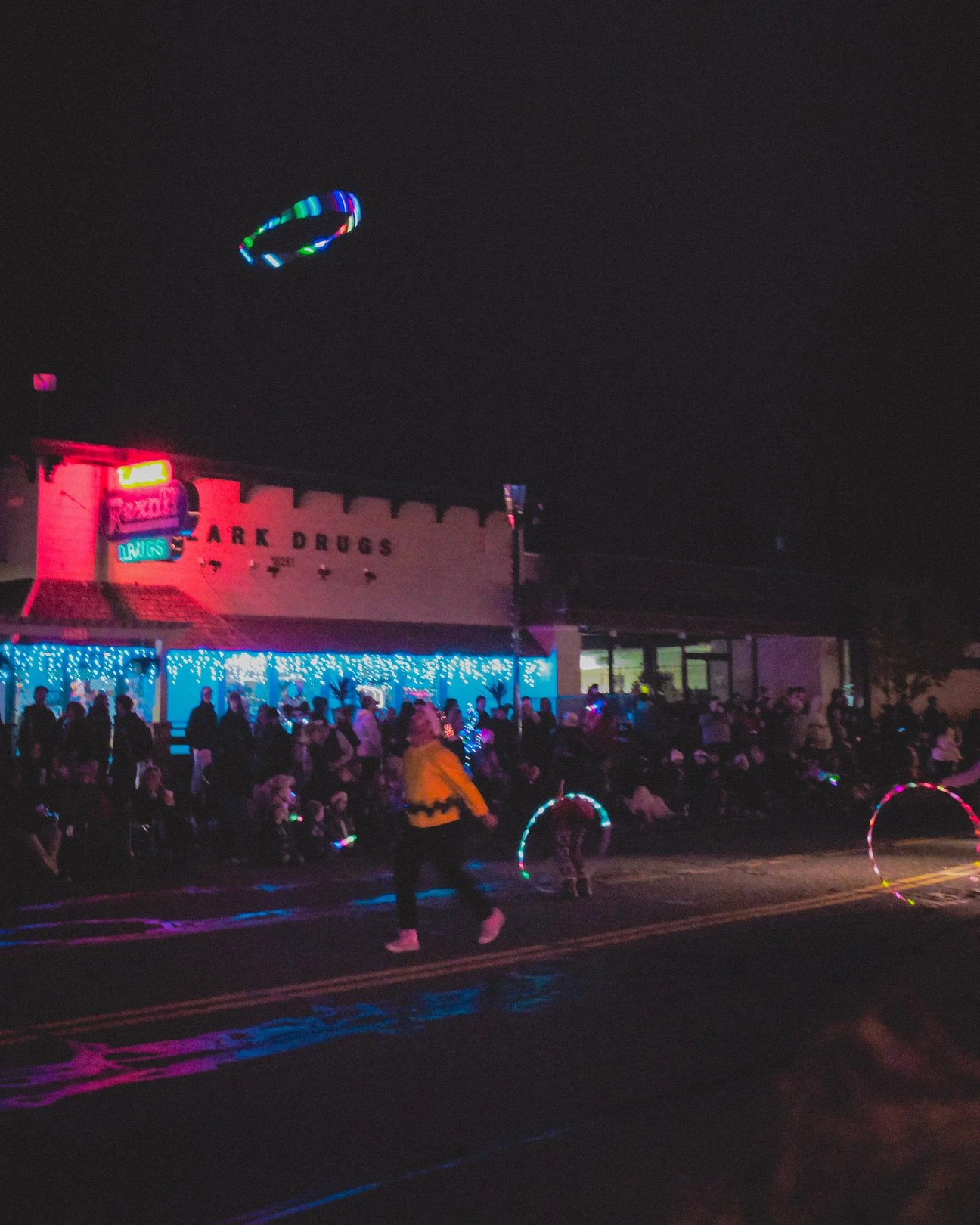 A vibrant nighttime scene featuring a crowd outside a colorful building illuminated by neon lights.