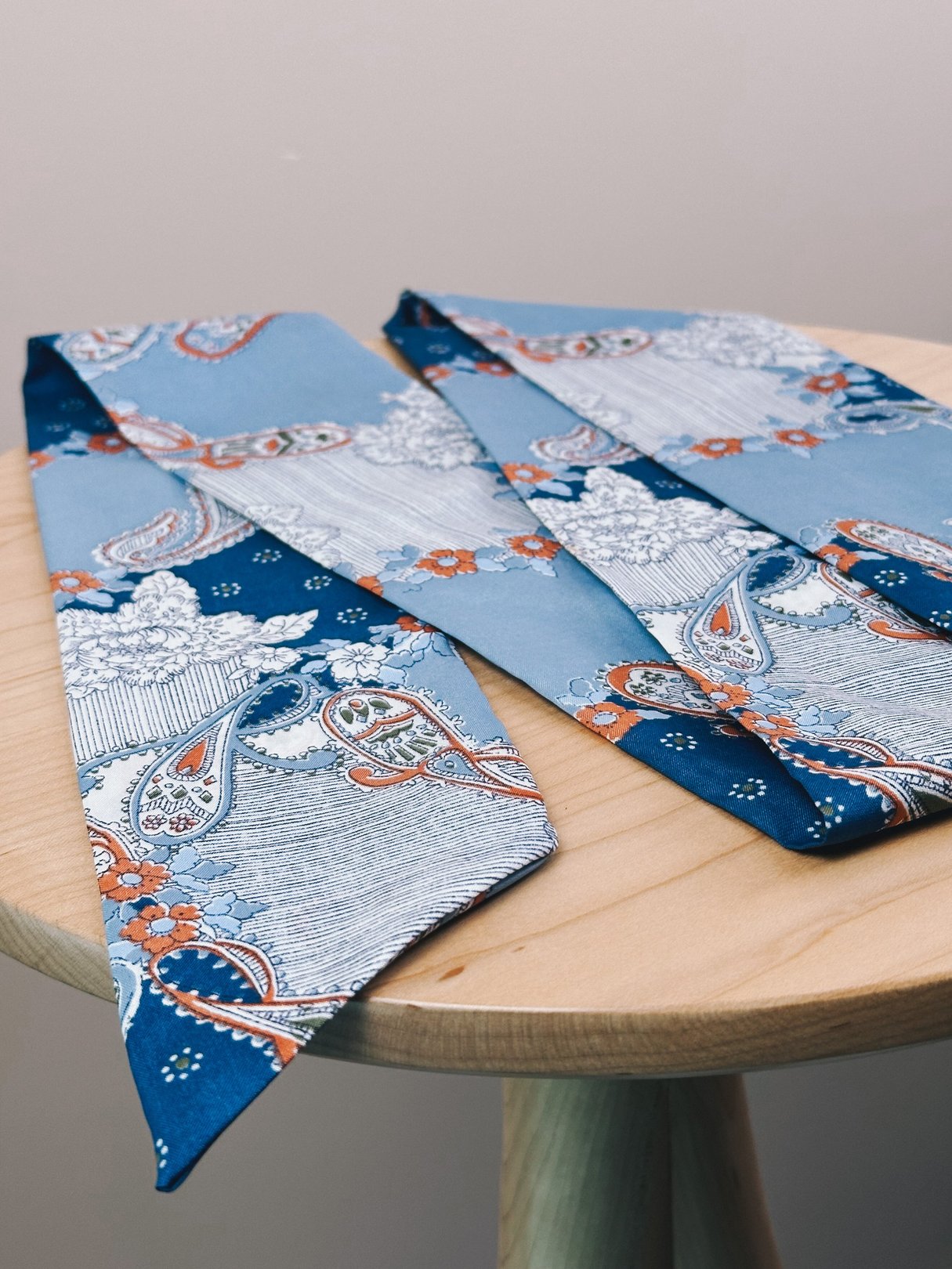 Light blue paisley scarf featuring intricate patterns in blue, white, and orange on a wooden surface.
