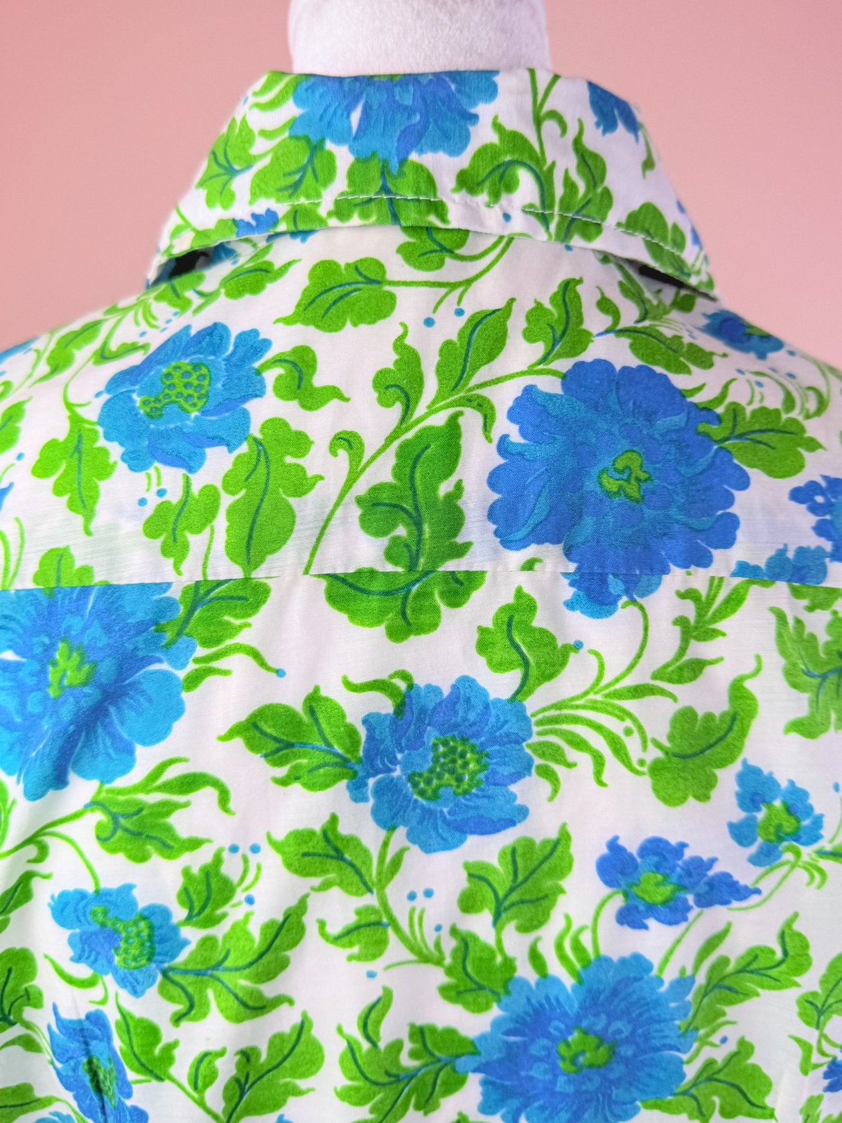 A 1960s women's dress featuring a white fabric adorned with large blue flowers and green leaf patterns.