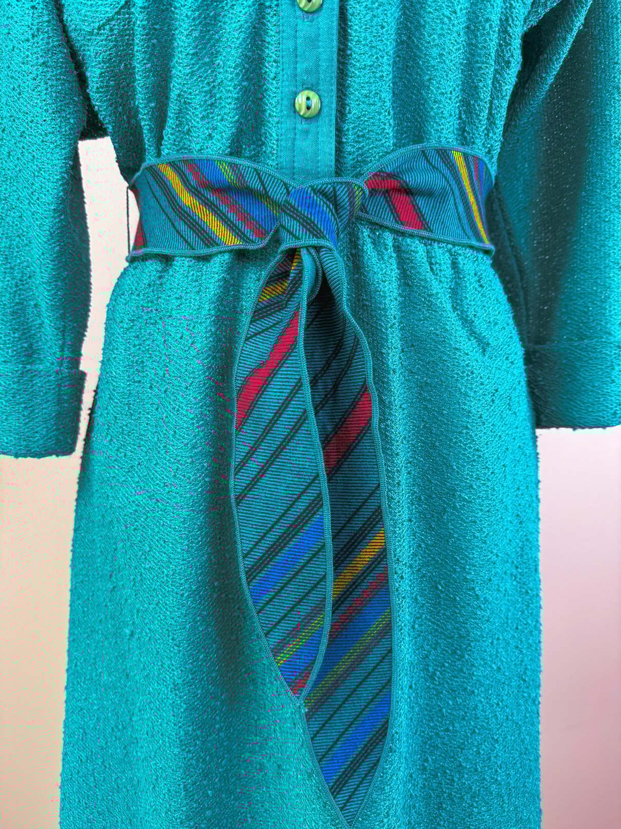 Teal 1980s women’s dress featuring a textured fabric and multicolored striped belt.