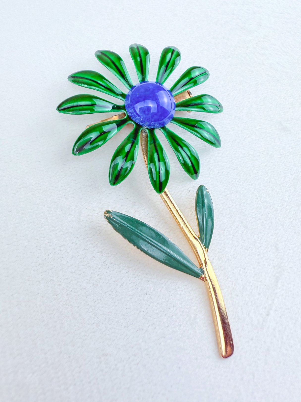 1960s blue and green flower-shaped brooch featuring a purple center.