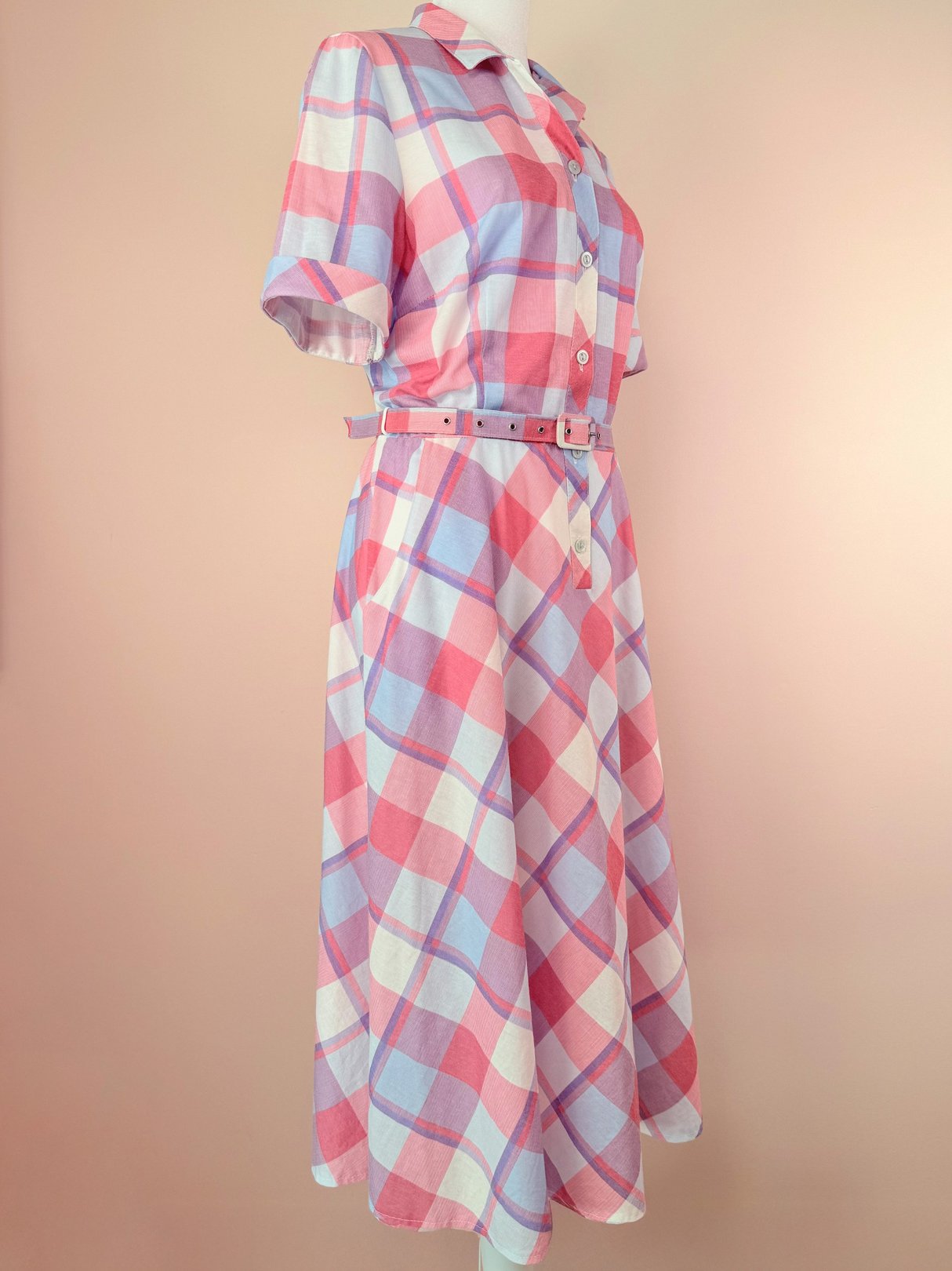 1950s women’s purple picnic plaid dress featuring a button-up front, short sleeves, and a belted waist.