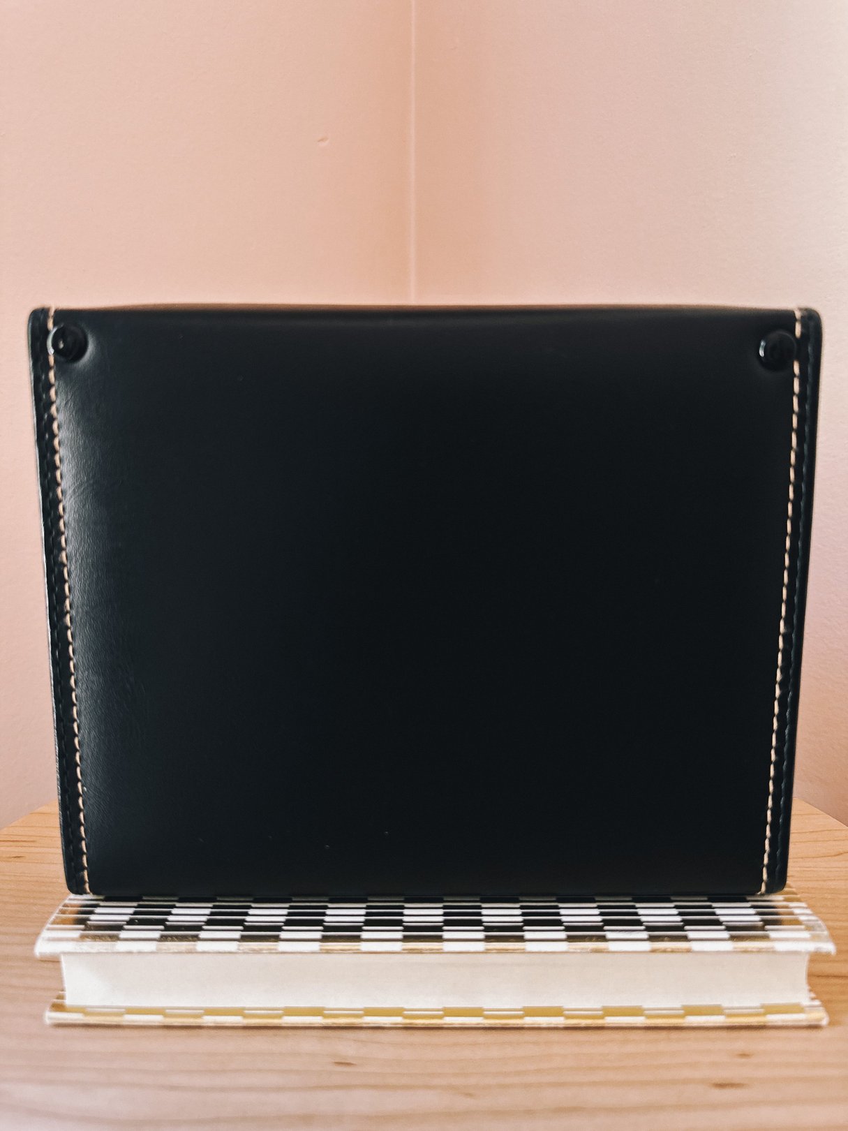 Black camera bag with a sleek design, featuring visible stitching and a retro aesthetic, placed on a checkered surface.