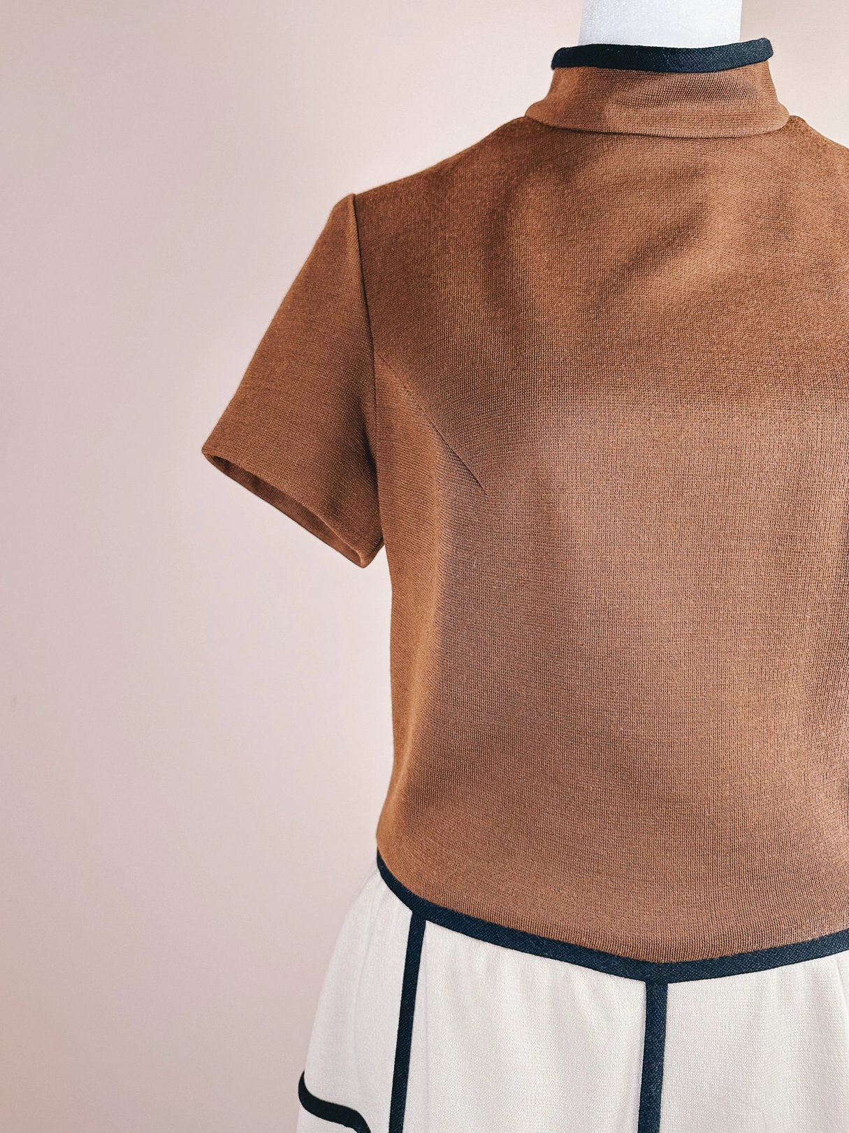 Short-sleeve brown top paired with white trousers featuring black trim.