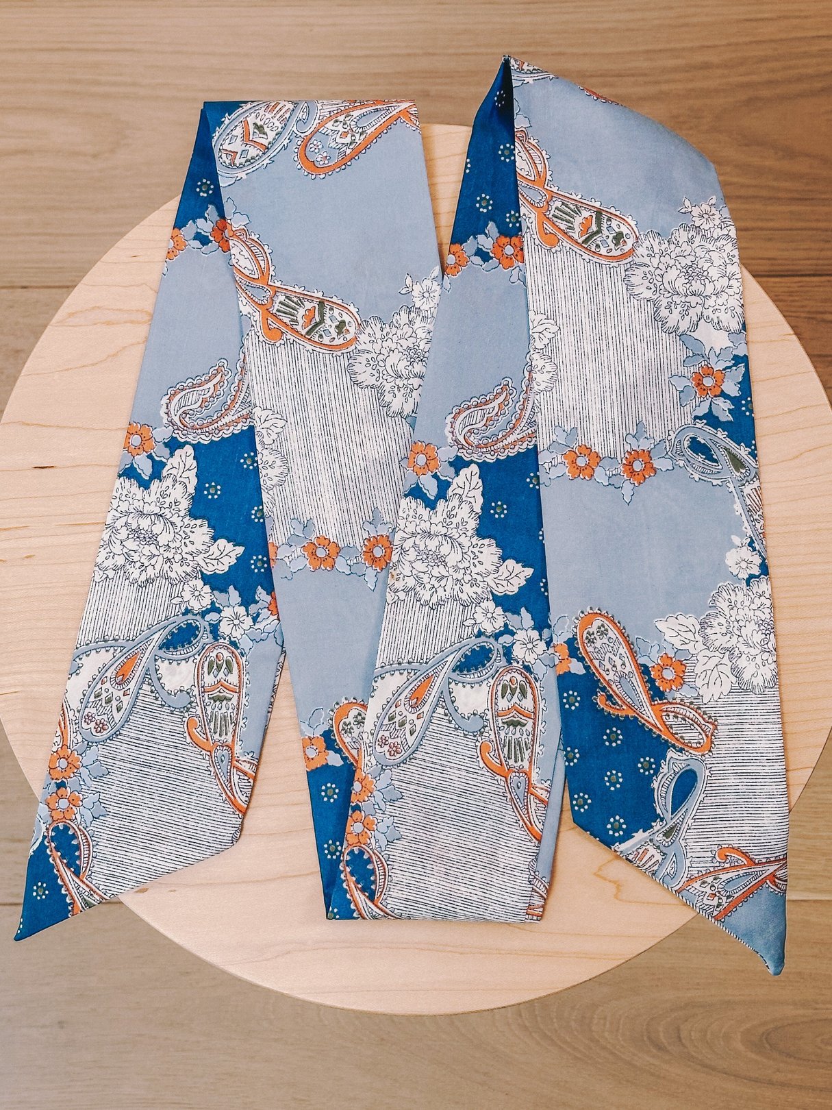Light blue 1970s women's paisley scarf featuring floral and paisley patterns in orange and white.