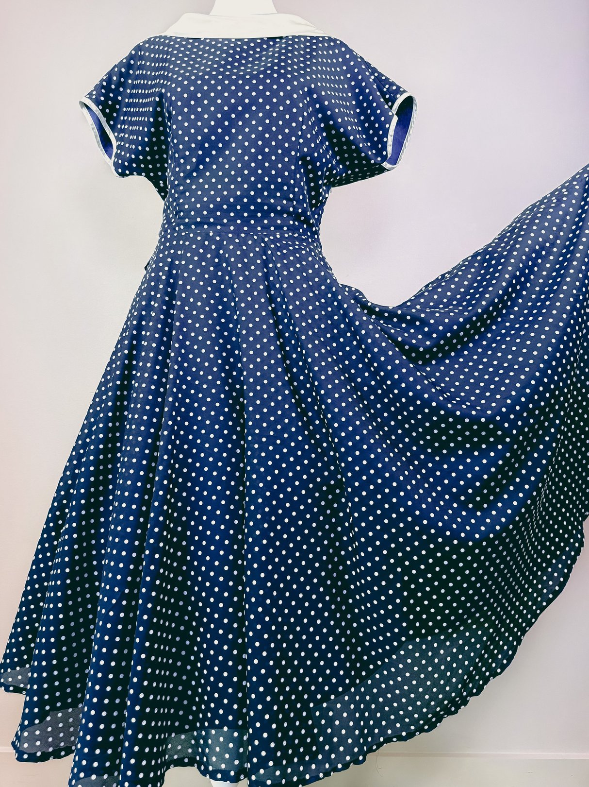 Navy blue 1950s women's dress featuring white polka dots and a flowing skirt.