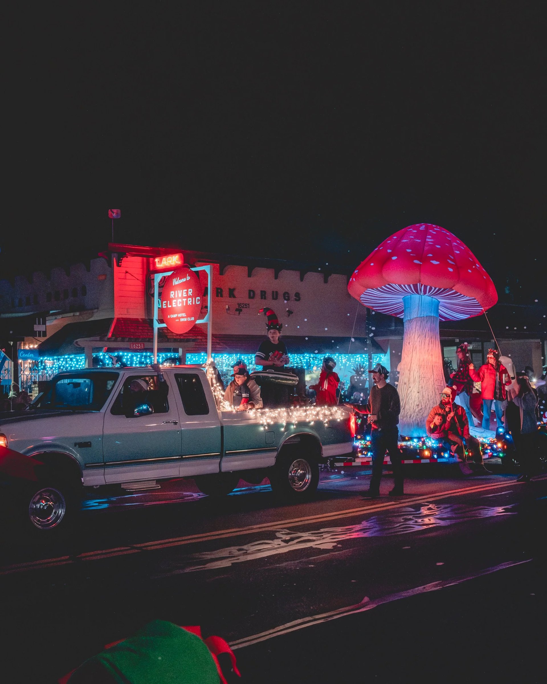 A decorated pickup truck with bright lights and a large mushroom statue in a festive parade setting.