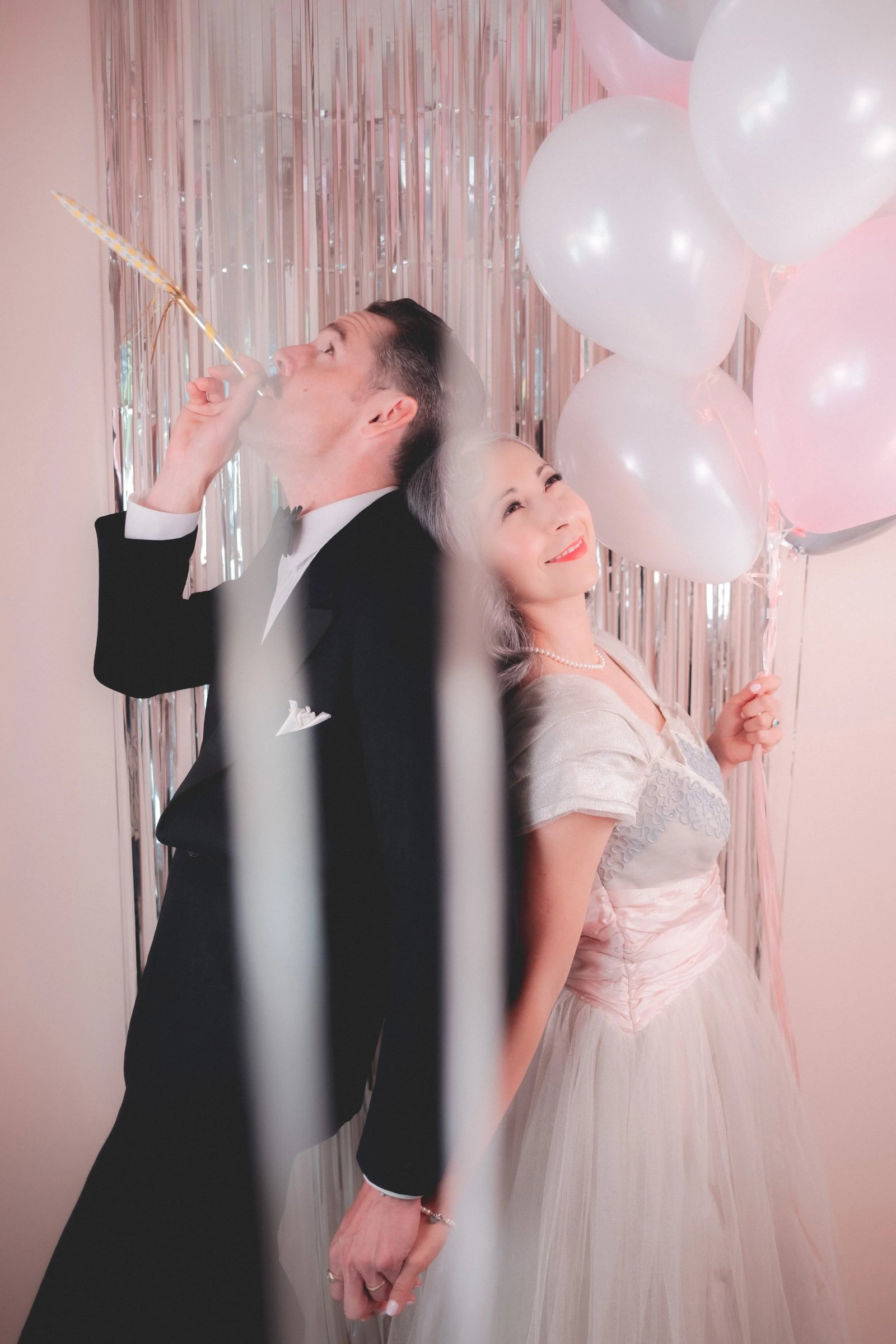A couple dressed elegantly celebrates with balloons in a festive setting.