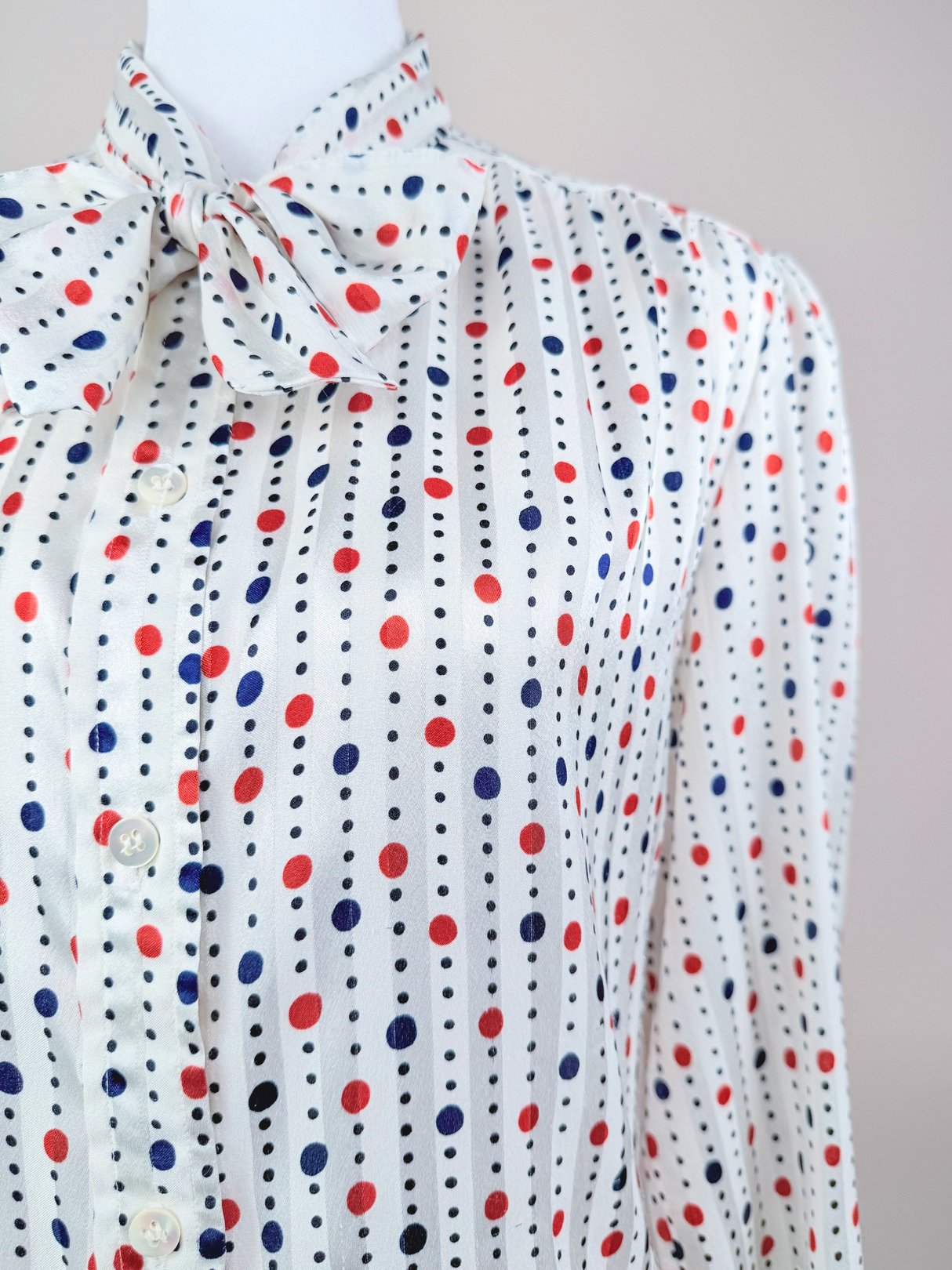 Red and white blouse featuring a polka dot pattern with a bow tie collar, reflecting 1980s women's fashion.