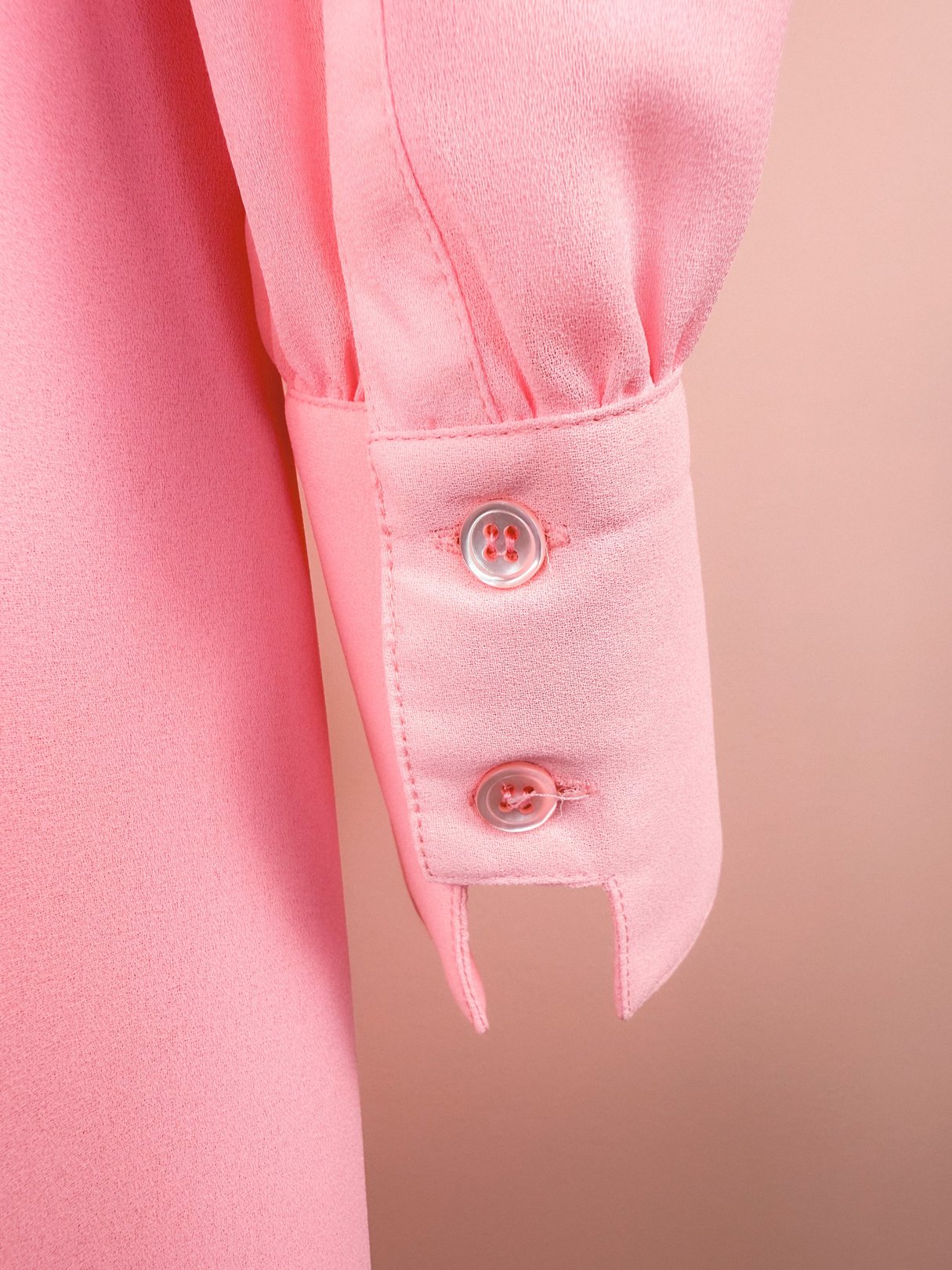 A close-up of a bubble gum pink dress sleeve featuring button details from the 1980s.